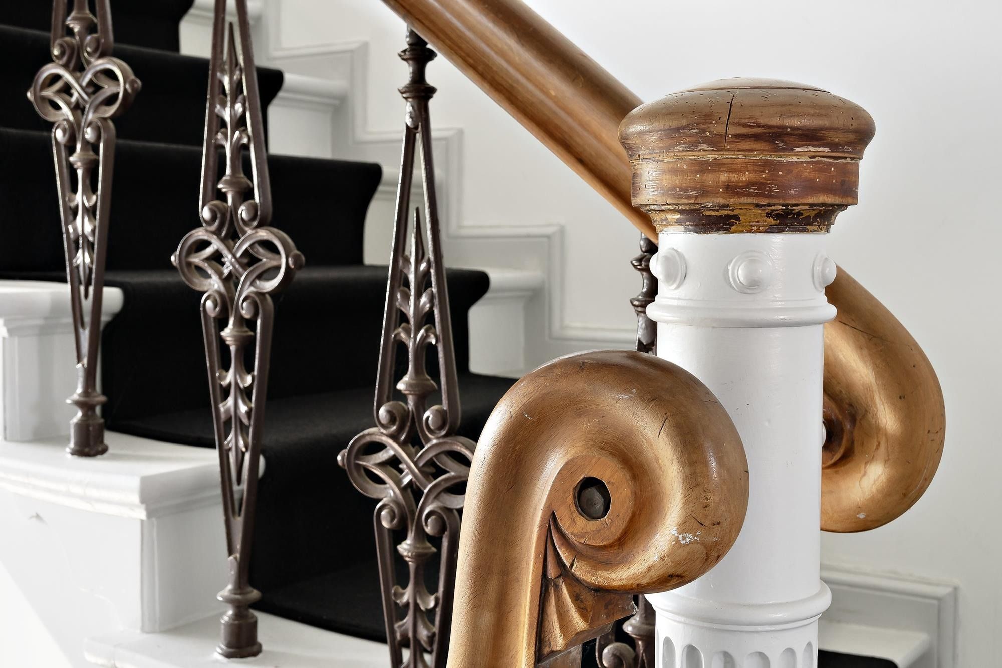 Elegant skråt gåhåndtag af bronze og træ med udskårne mønstre og forgyldte spidse ender og en hvid marmorsøjle