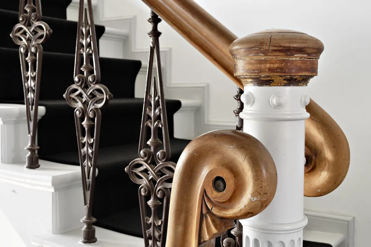Elegant skråt gåhåndtag af bronze og træ med udskårne mønstre og forgyldte spidse ender og en hvid marmorsøjle