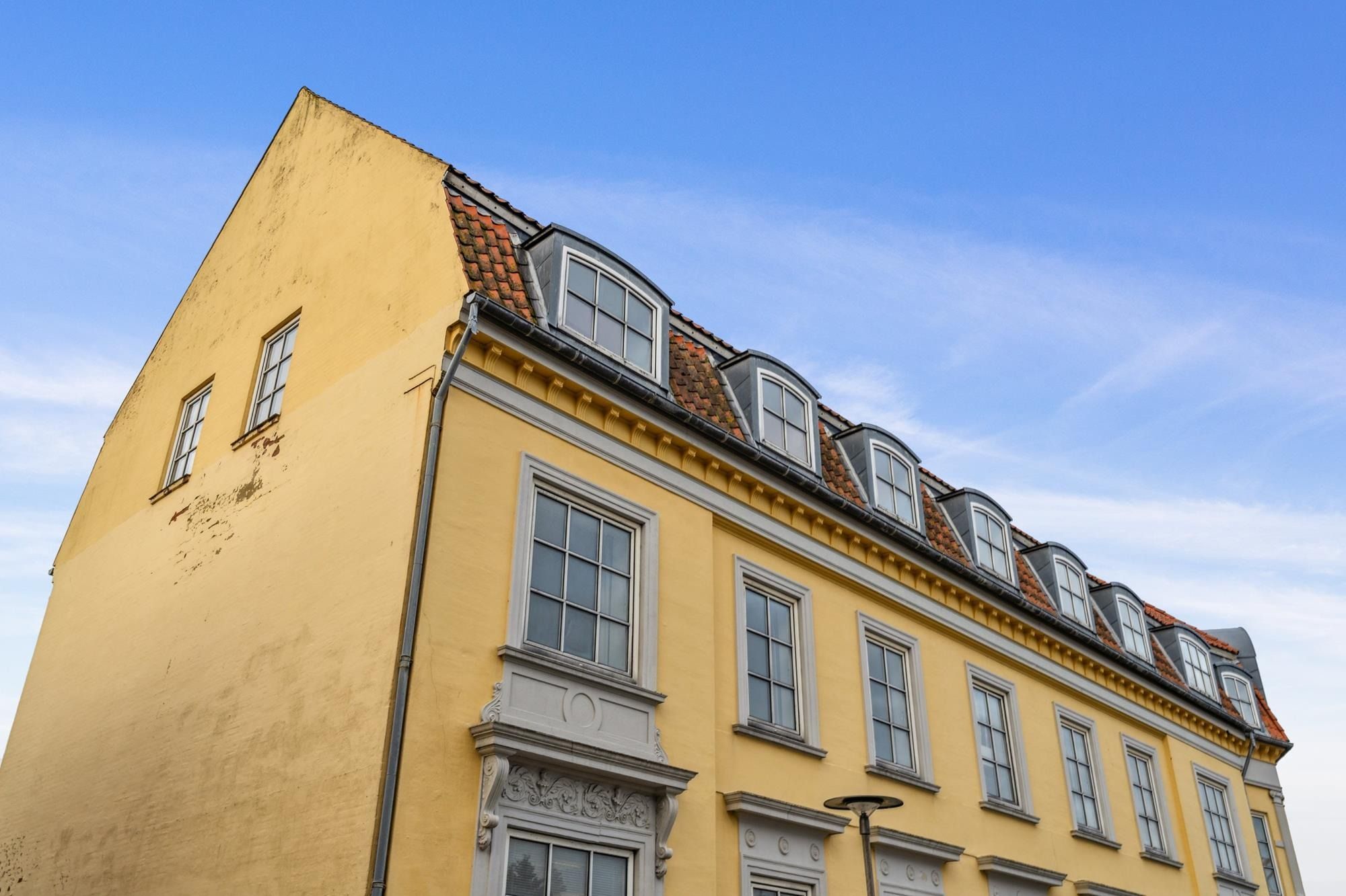 Gult bygningsværk med mange vinduer og en facade i nyklassisk stil under en tydelig himmel med skyer