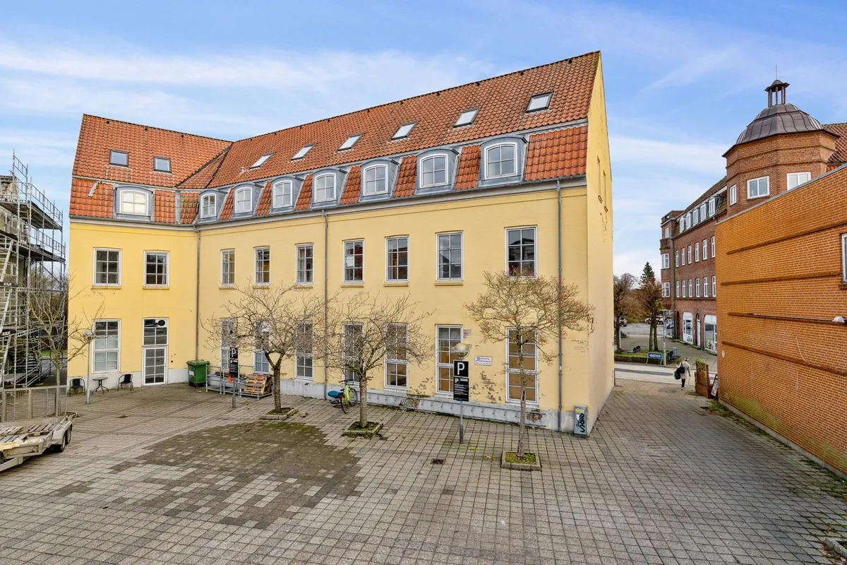 Gammel gule bygning med parkeringsskilt og 2 træer og 2 stolpe på forsiden.