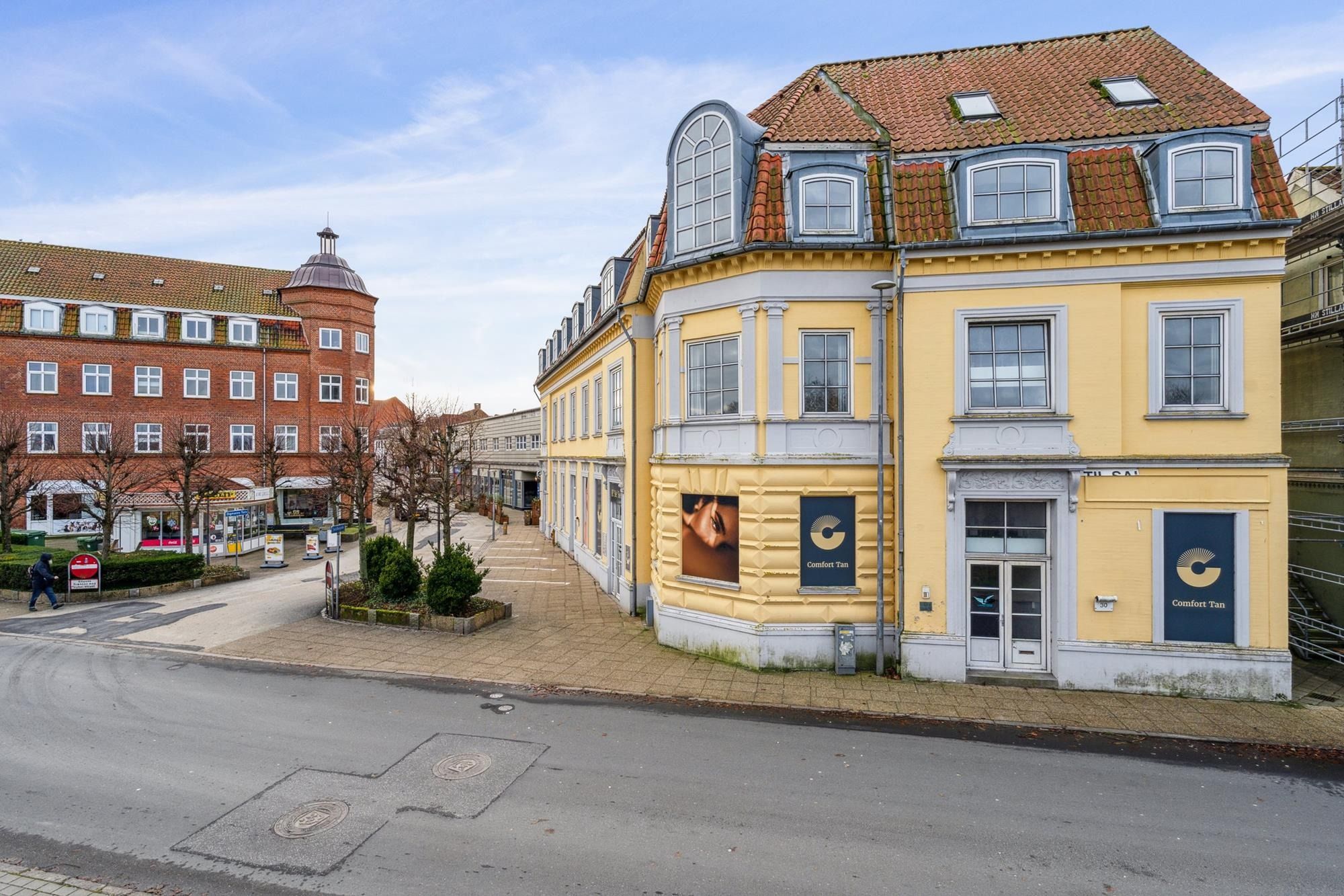 Bygning med facademaling og reklameskilte, mens en person går på gågaden. Butiksvinduer og søjler langs siderne.