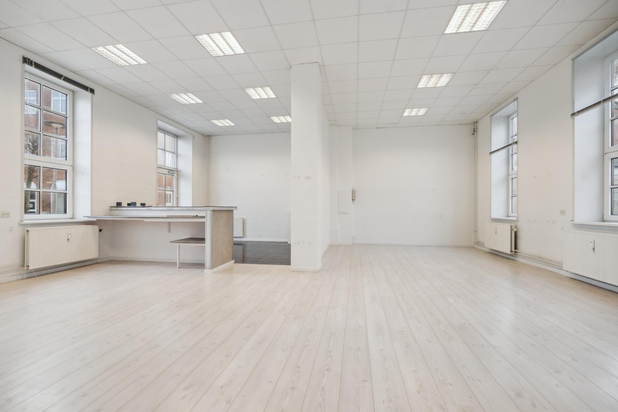 Store lokaler med hvide vægge, lyse lofter, lysegulve og lyseruder og vinduer. Lokaler med radiatorer og stol med skrivebord.