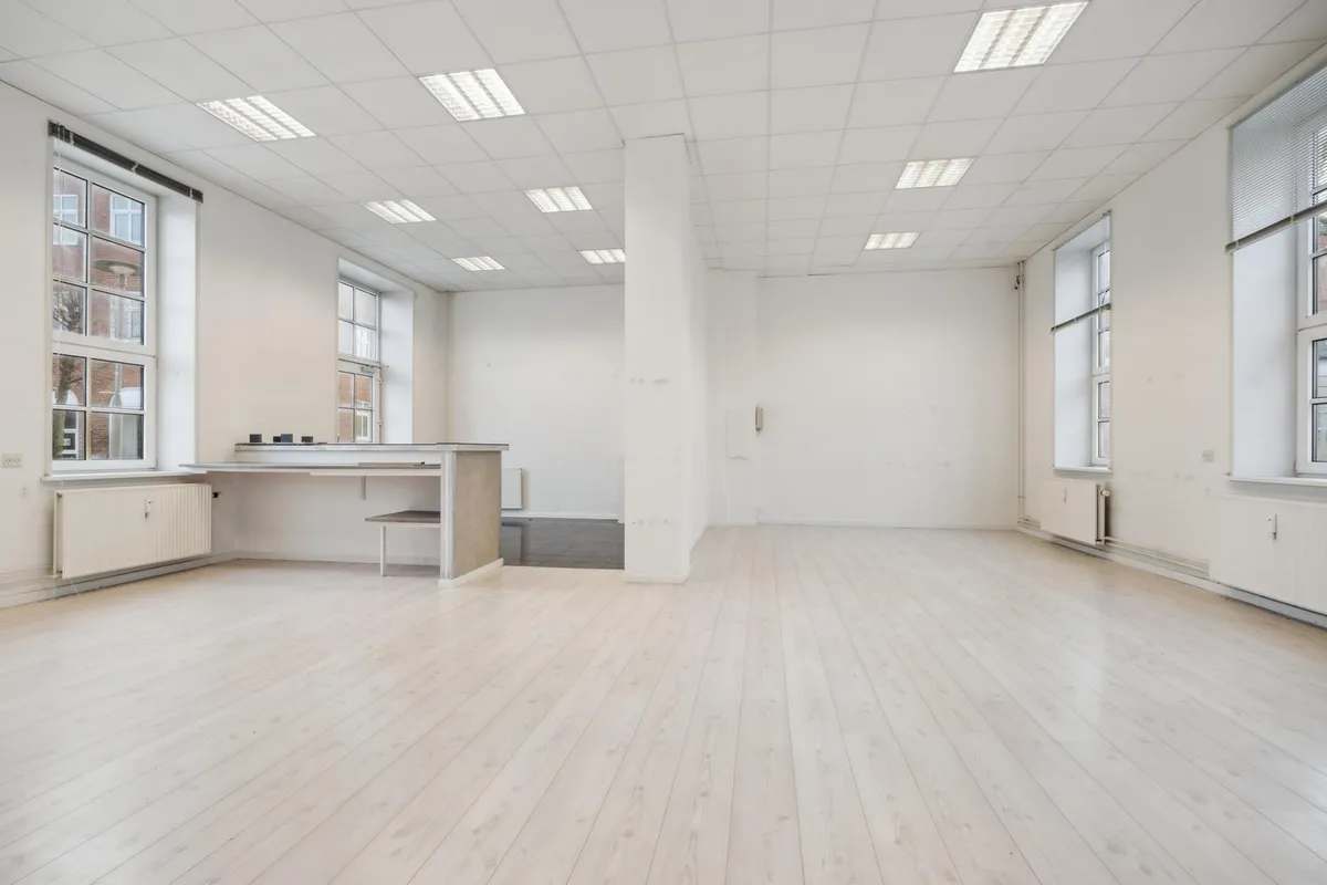 Store lokaler med hvide vægge, lyse lofter, lysegulve og lyseruder og vinduer. Lokaler med radiatorer og stol med skrivebord.