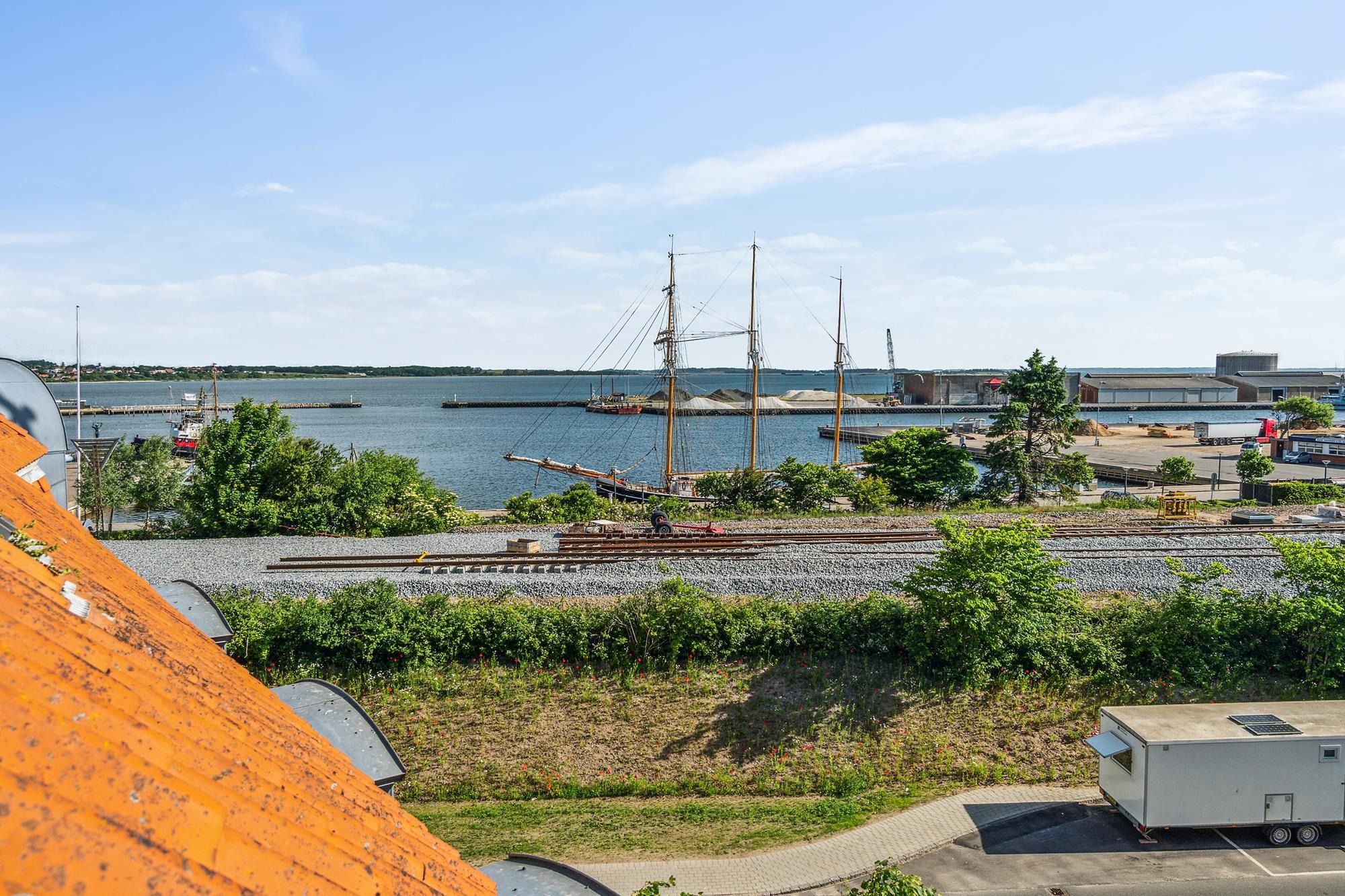 Et højt op mod himlen med sejlbåd og skibsværft, havneområde med søfart og transport, grønne planter og buske, en huslig
