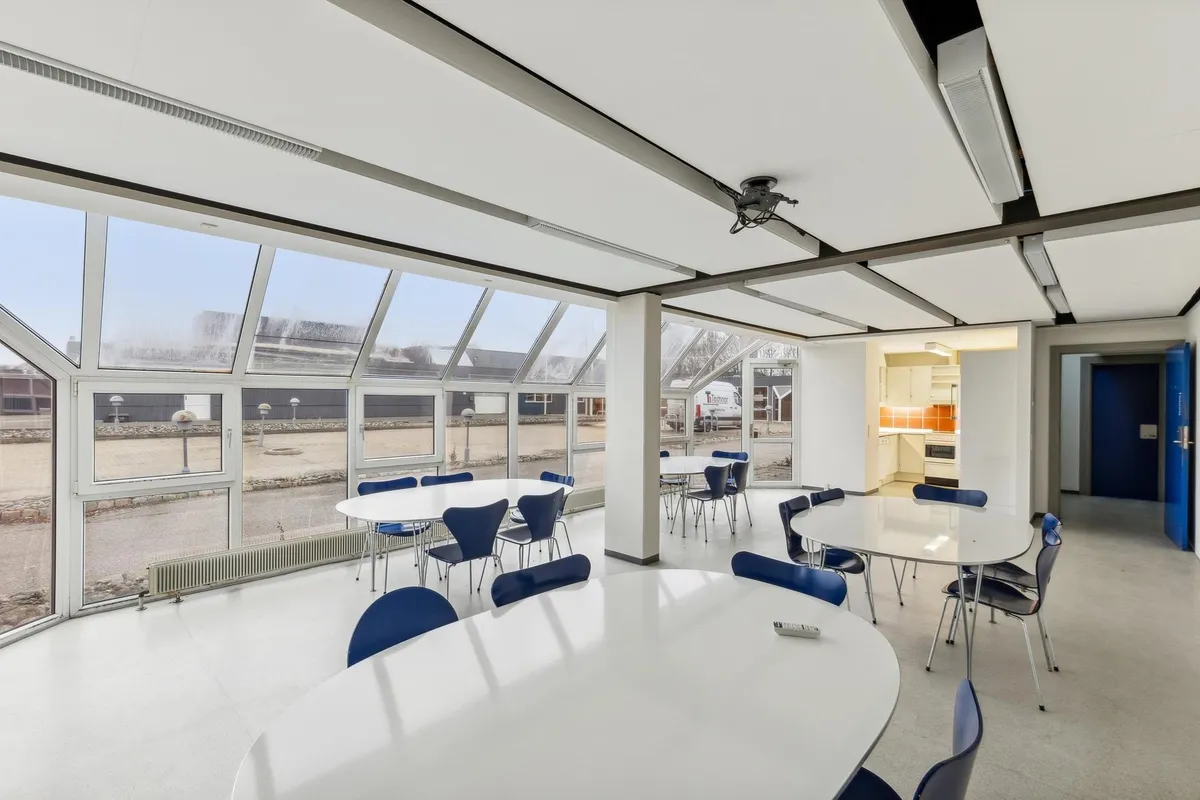 Konferenslokal med store vinduer og hvide møbler samt højt loft med hvide loftbelægninger og projektor