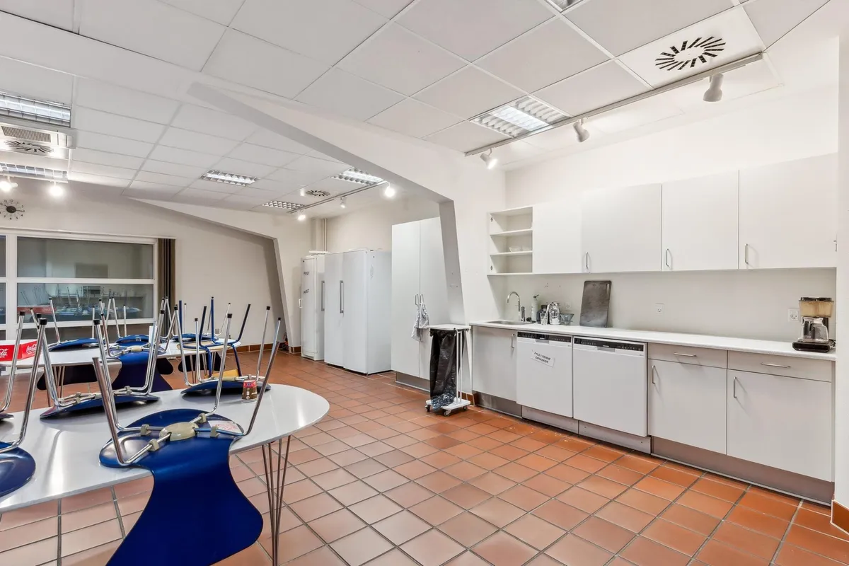 En tom køkken med moderne design, lyse hvide vægge, trægulv og høje lofter med indbyggede lamper og et stående køleskab