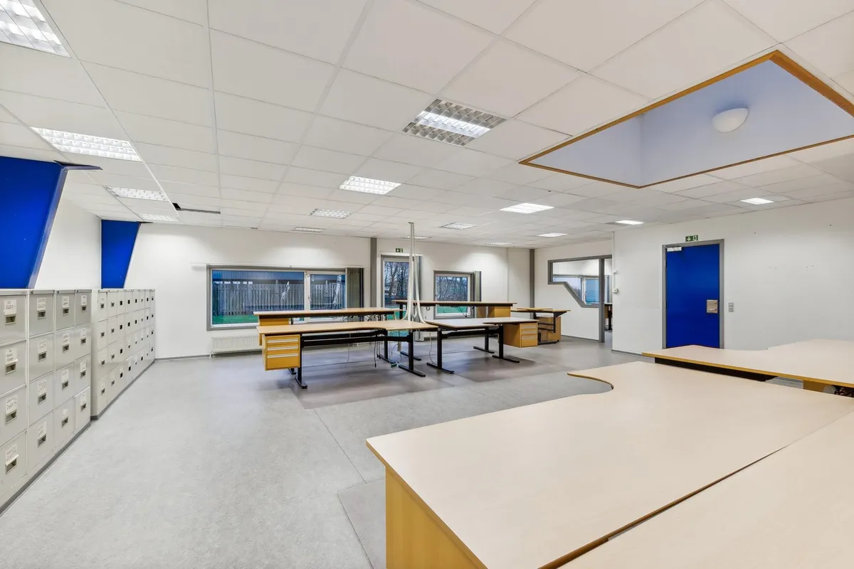 Inde i et kontorlokum er der en stor mængde borde og stolpe, hvor de er arrangeret i en U-form. Loftet er hvidt med flere