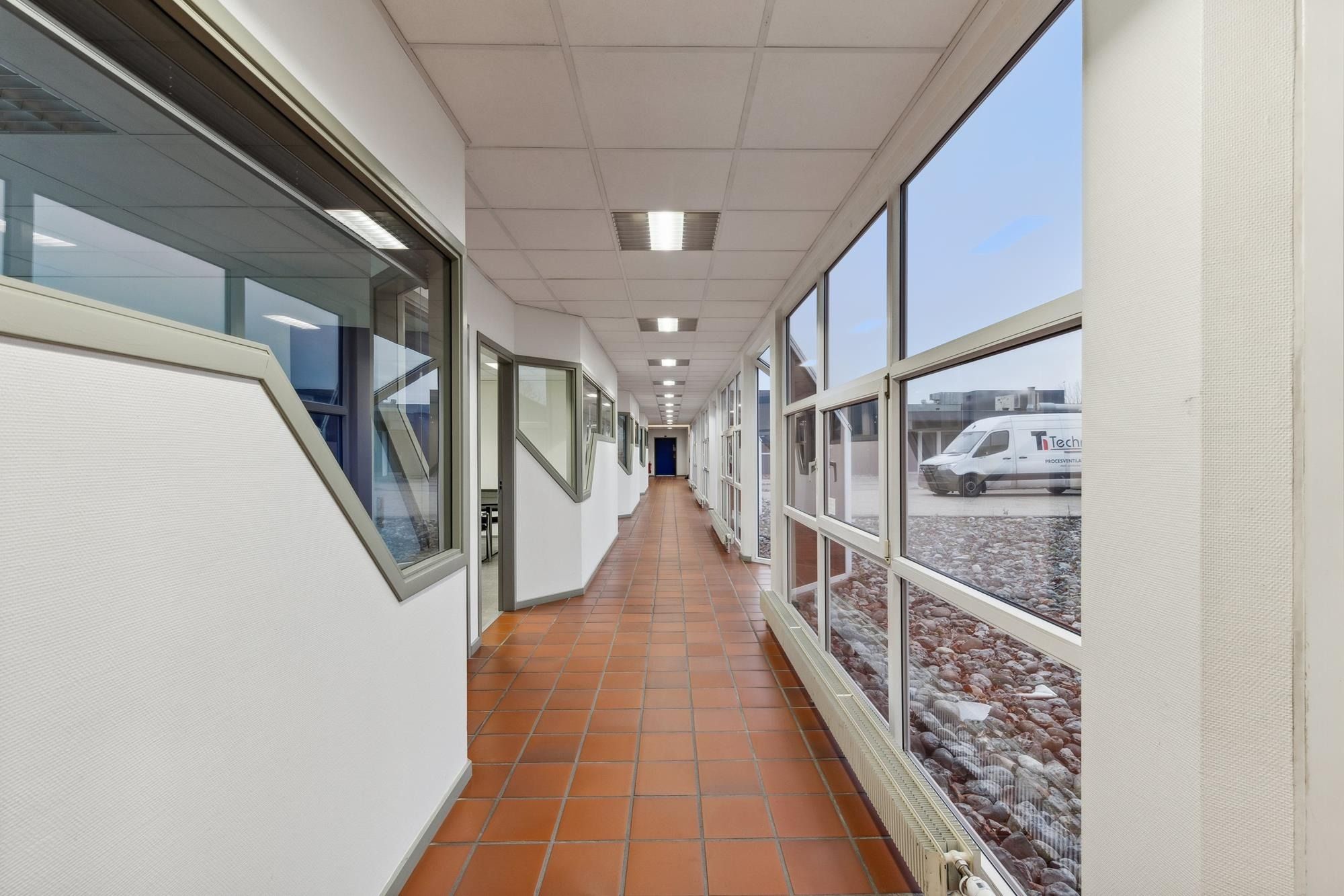 En hal med lyserøde klinkergulve og glasvinduer der går langs hele væggen