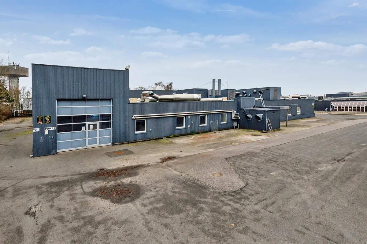 Produktionsbygning med dobbeltdør og port, hvor det ser ud til, at der er en række produktionsbygninger bagved og et tårn i