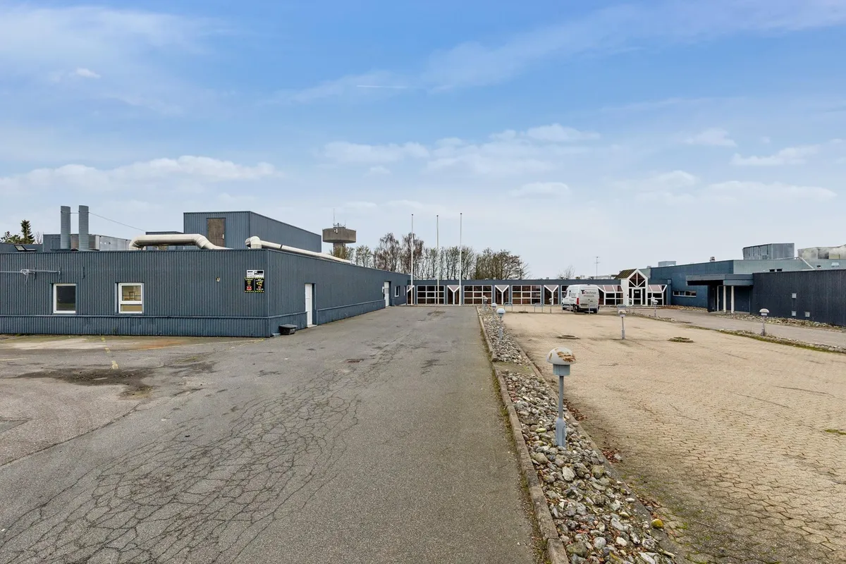 Et stort, gråt bygningskompleks med mange vinduer og et stort parkeringsområde foran