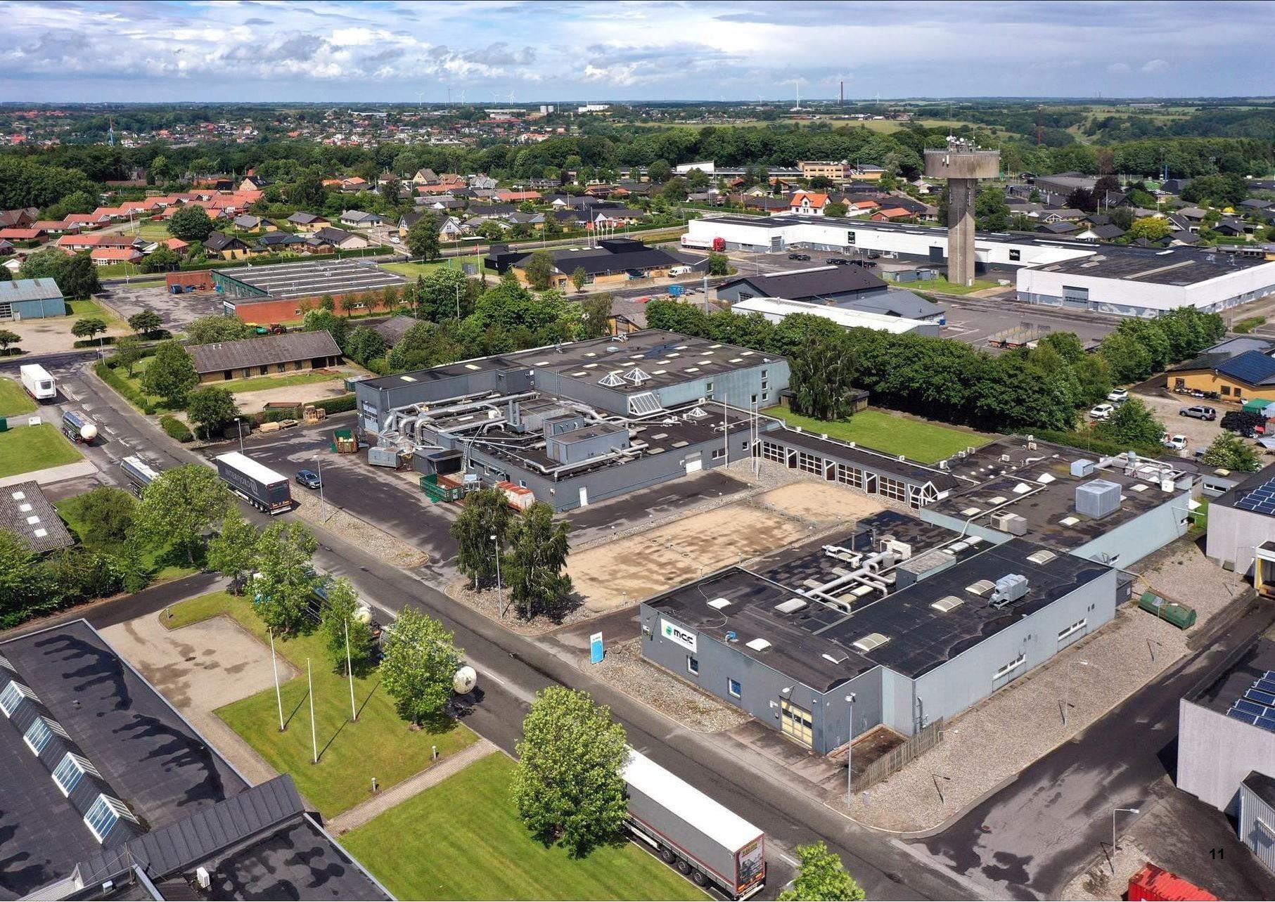 En industripark med flere bygninger og en stor parkeringsplads, to vogne og et tårn i baggrunden