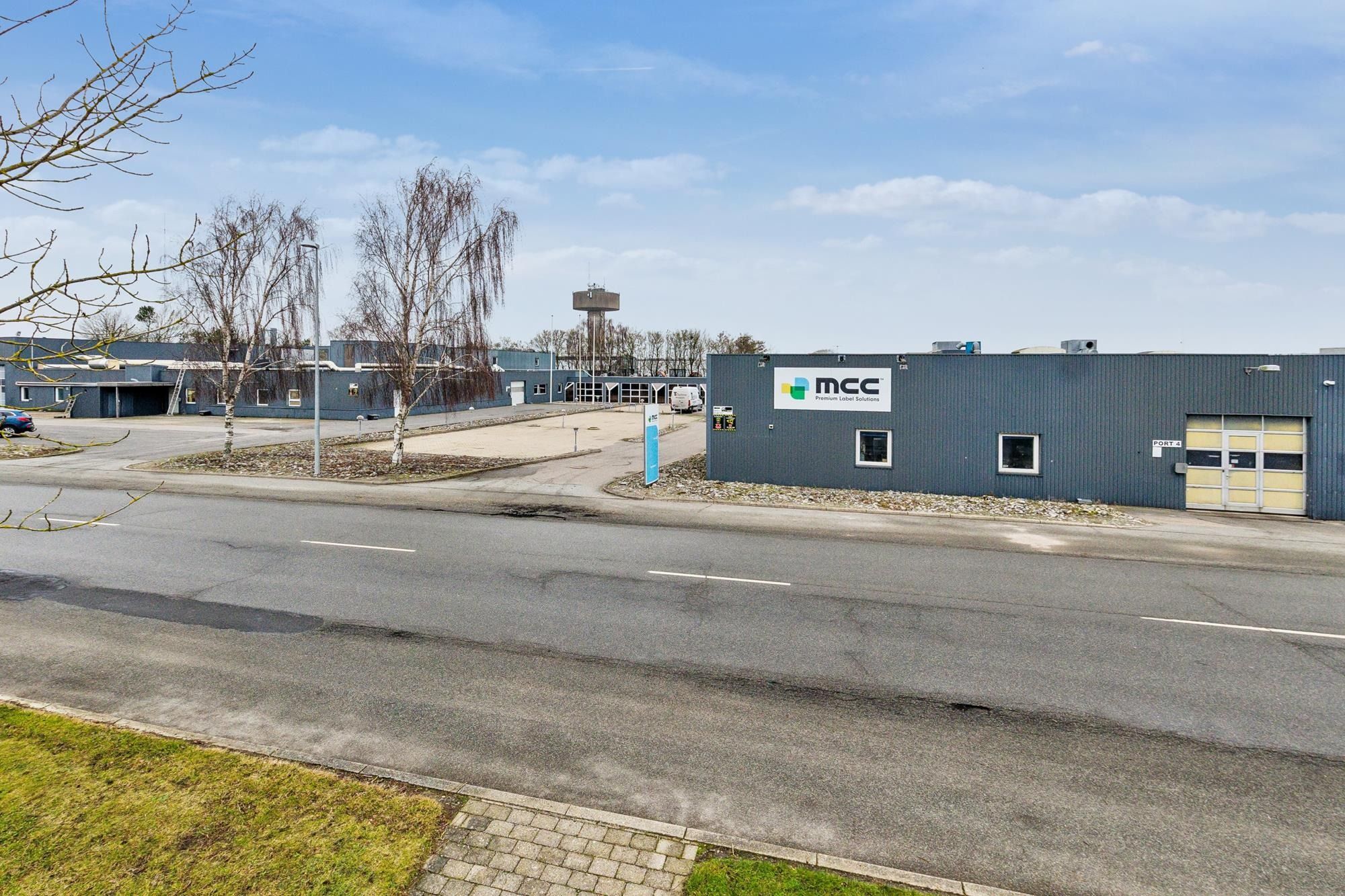 Fabrik og parkeringsplads med en stor bygning og teksten MCC Premium Label Solutions på væggen