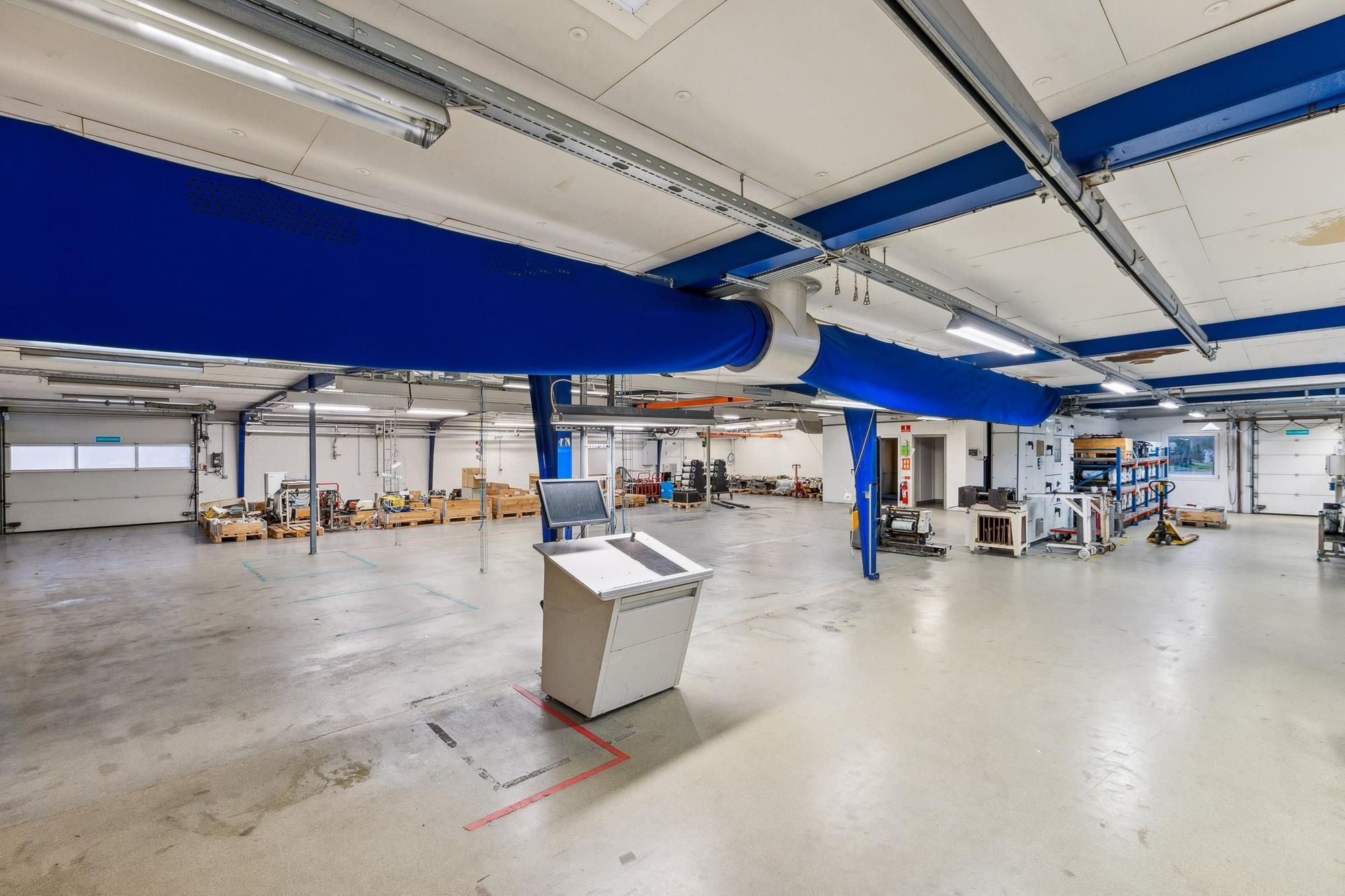 Et stort industriområde med højloftede lofter og mængder af udstyr og maskiner samt et stort skrivebord i midten af rummet