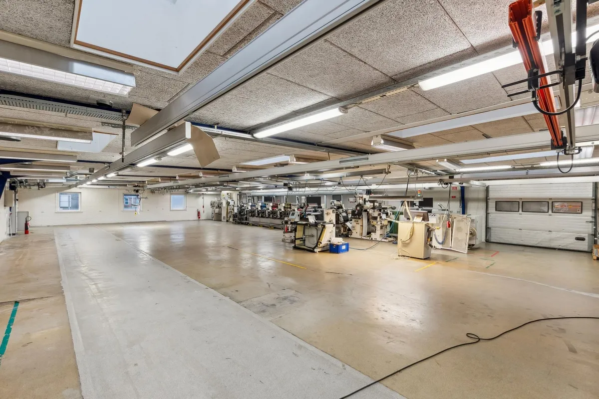 Fabrik med lysekroner og flere maskiner i ro. Der er røde brandslukkere og et hvidt gulv