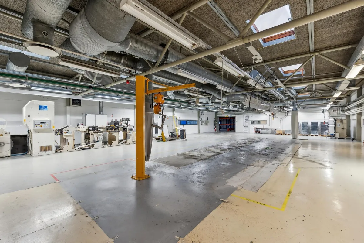 Fabrik med maskiner og store vinduer og et stort åbent areal med gult sikkerhedsbånd