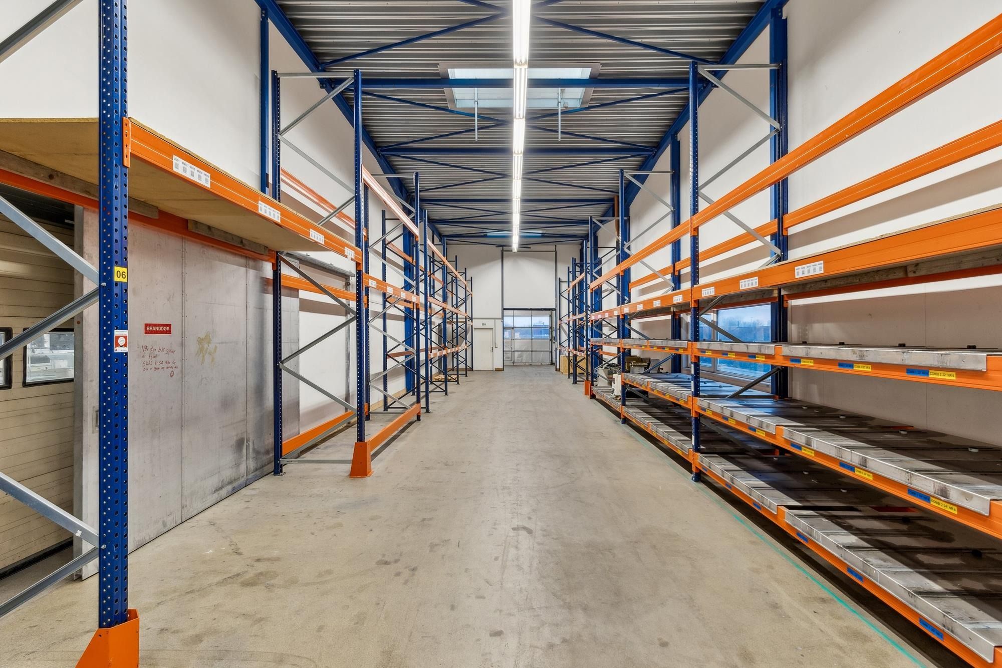 Lager med gulvmonterede lagerreoler og gulvmonterede paletter samt glasdøre og et skyloft med lysepaneler