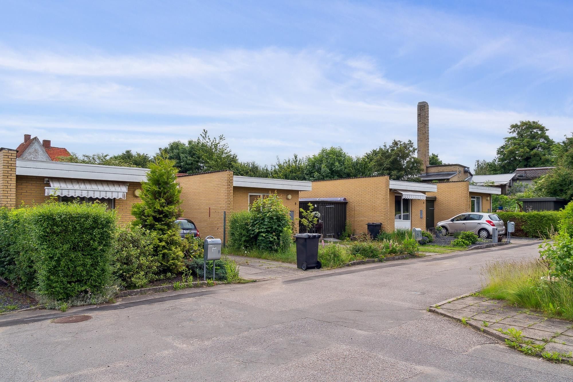 Moderne rækkehuse med røde tag og hvide gardiner og udsigt til en stor gårdhave med grønne buske og et parkerede biler