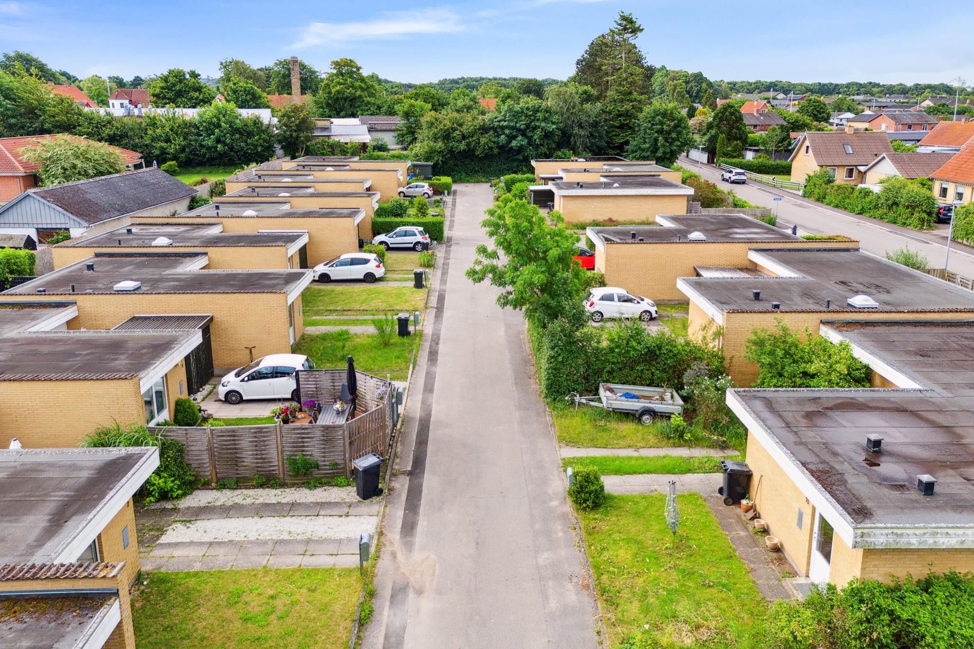 16 moderne rækkehuse i en lille bydel med en lang vej og forskellige biler parkeret langs vejen