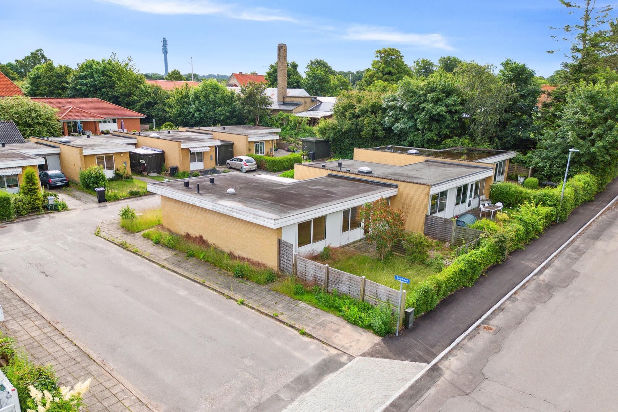 Moderne rækkehuse med garager og haver, gader og parkerede biler, tætte grønne træer og solrige himmel