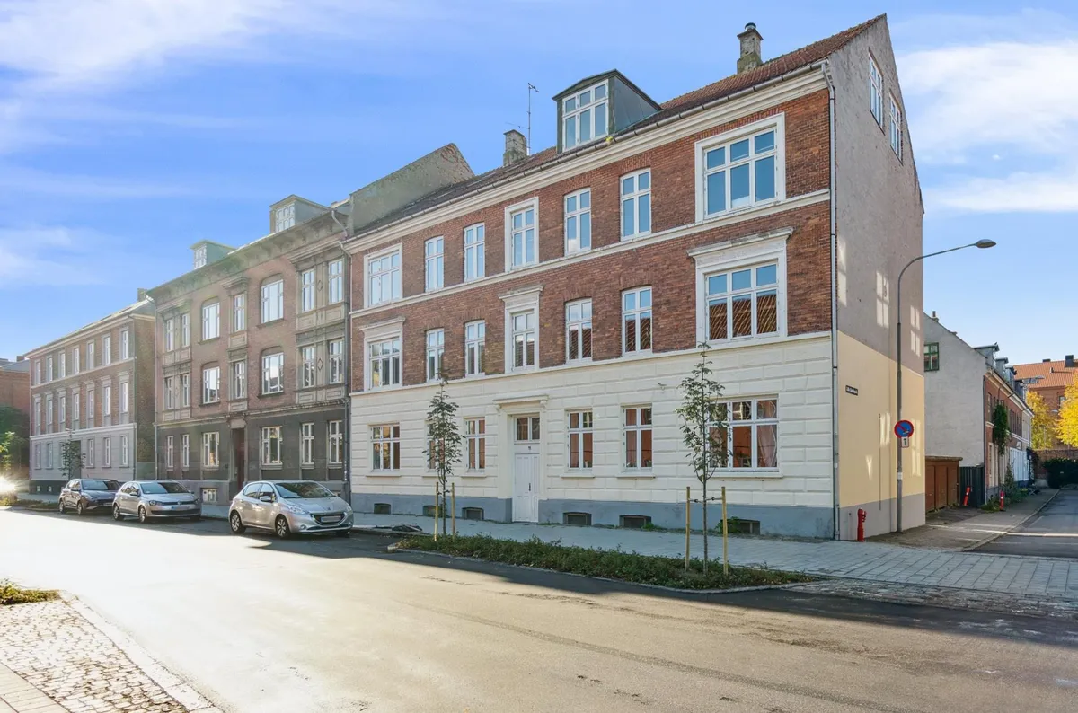 En smuk ejendom med røde mursten og hvide detaljer står på en gade i en lille by med tre parkerede biler og en søjle