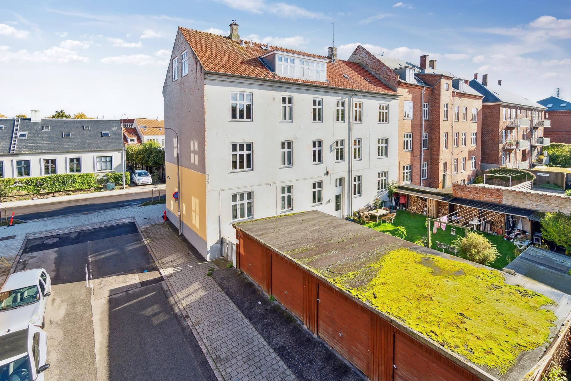 Boliger med udsigt til grønne haver og røde murstenshuse. Parkerede biler og lyserøde tagdækninger. Grønne planter og haver