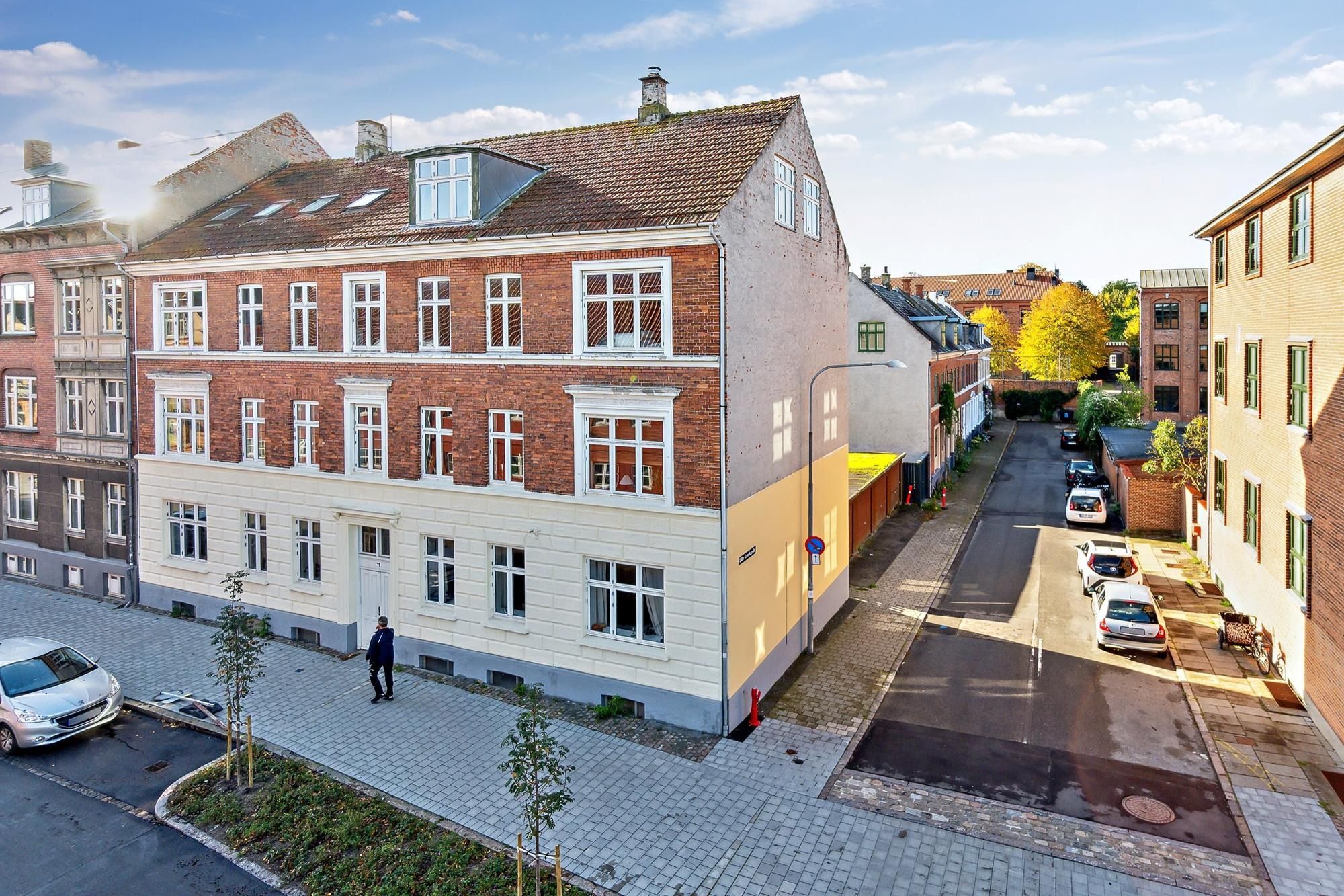 Forsiden af småhusejendom med syv boliger og tre parkerede biler på gågaden udenfor engangsvej