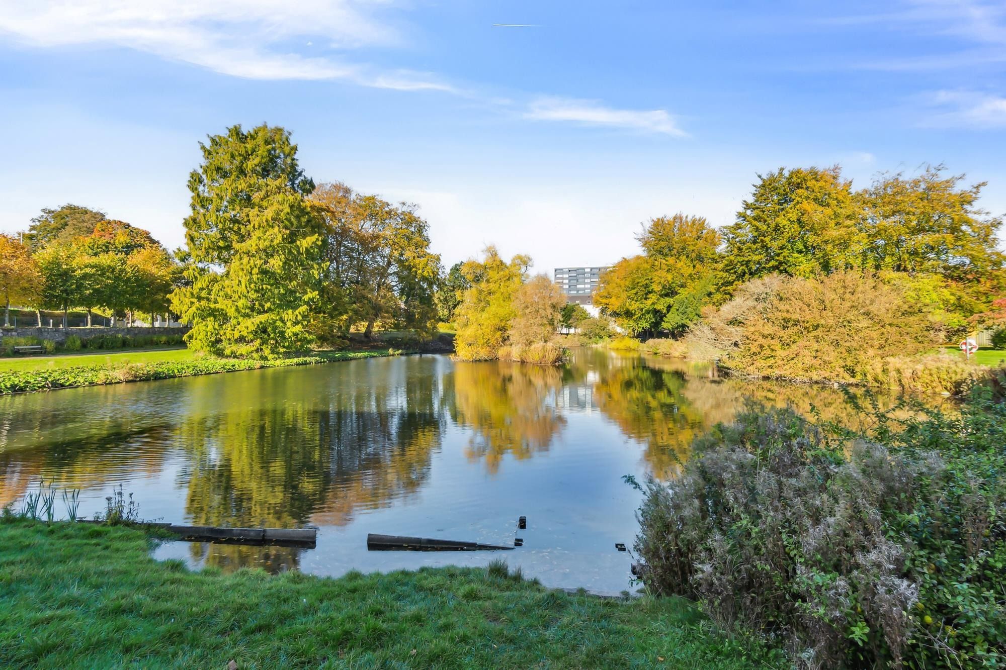 Flod med fredfyldt vand og dyb bladløs skov. Lys himmel med skyer og en lille bygning i baggrunden. Flodbredden er dækket af