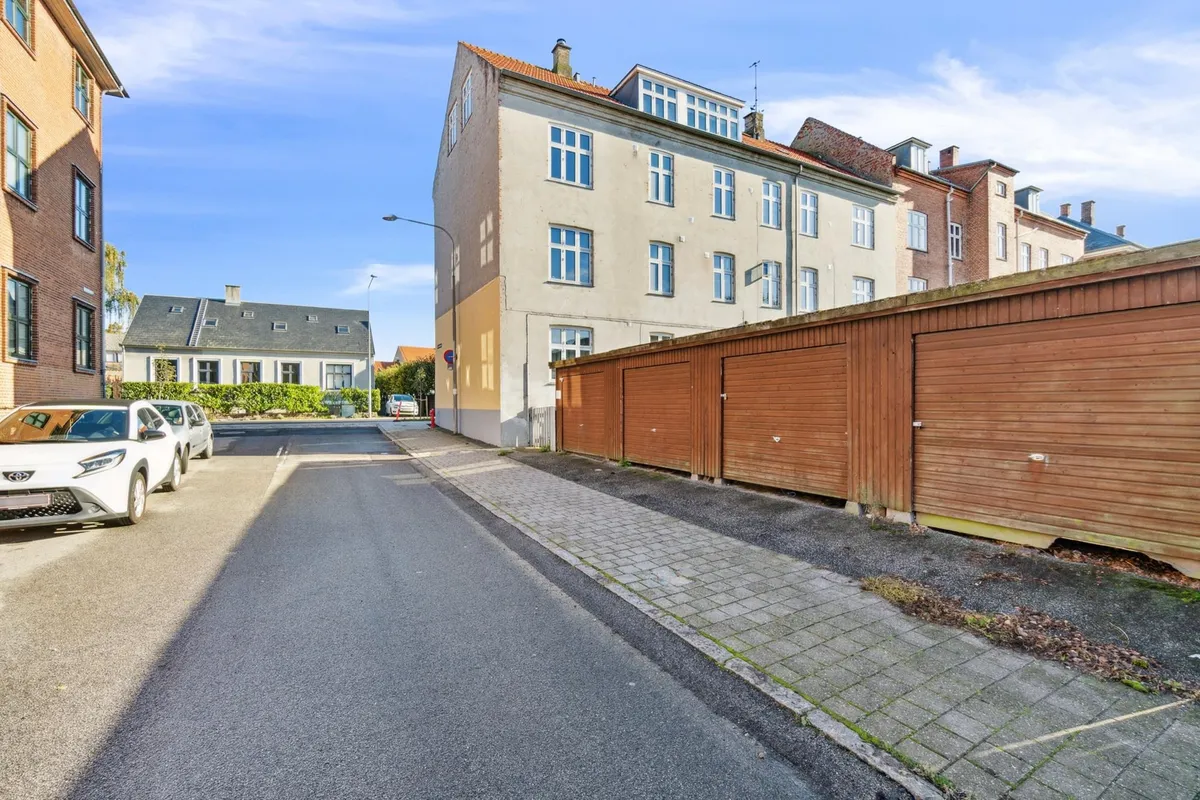 Vej med biler parkeret og røde murstensbygninger med flere vinduer i baggrunden