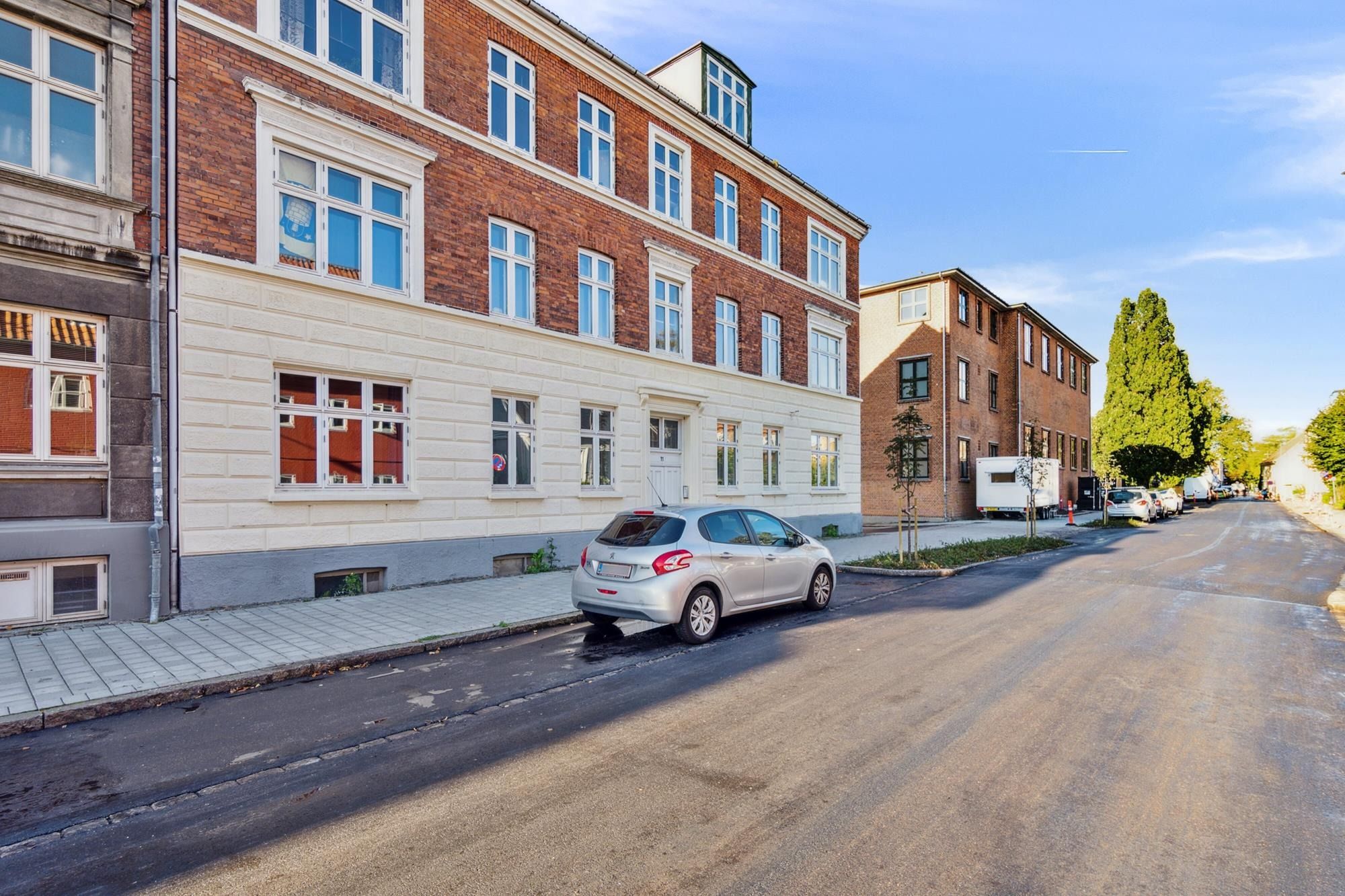 En lille parkeret Peugeot-bil med røde forlygter og hvide forlygter står parkeret på en tom gade i Lundegade i København