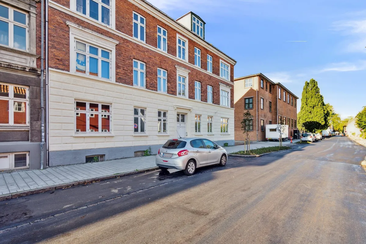 En lille parkeret Peugeot-bil med røde forlygter og hvide forlygter står parkeret på en tom gade i Lundegade i København