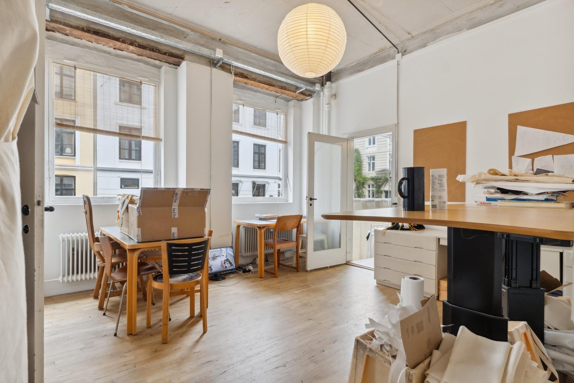 Rummelig stue med masser af plads og højt til loftet, fuld af møbler og ting, som skal pakke. Rundt lampe lyser og giver