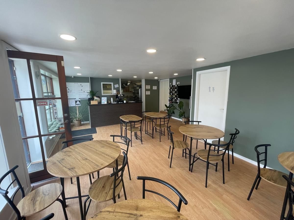 Et café med runde træborde og stole samt en kasse med vinflasker, der står i et hjørne