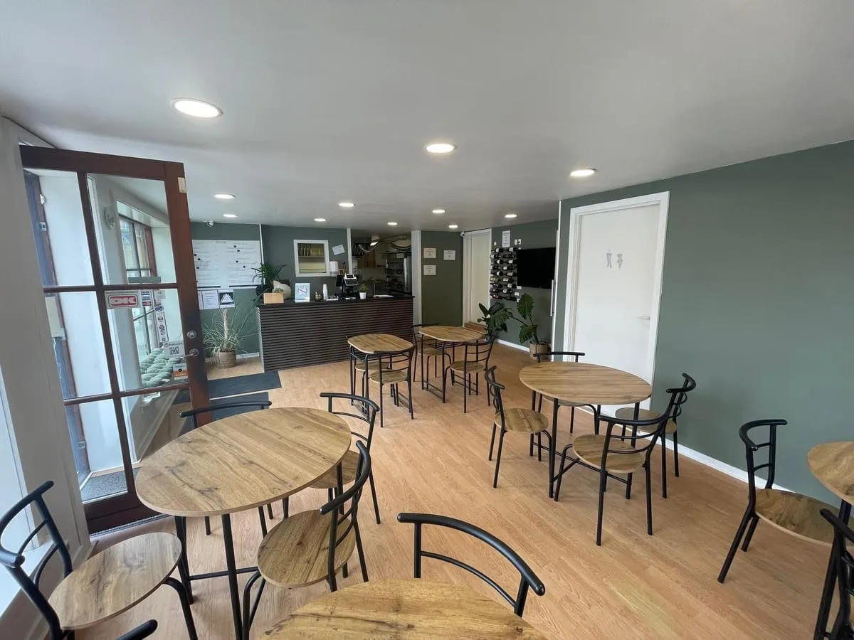 Et café med runde træborde og stole samt en kasse med vinflasker, der står i et hjørne