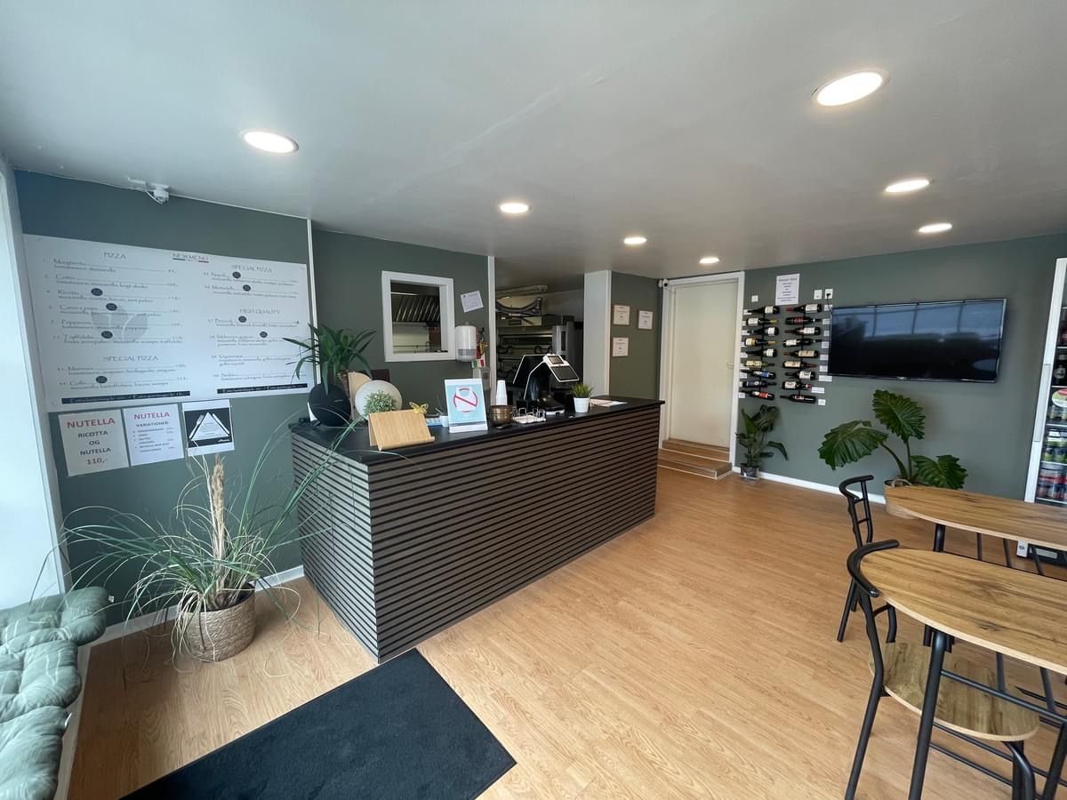 Et moderne kontor med en brun reception, hvor en plante og en tv-skærm er placeret. Der er en menuvæg og en dør, der fører