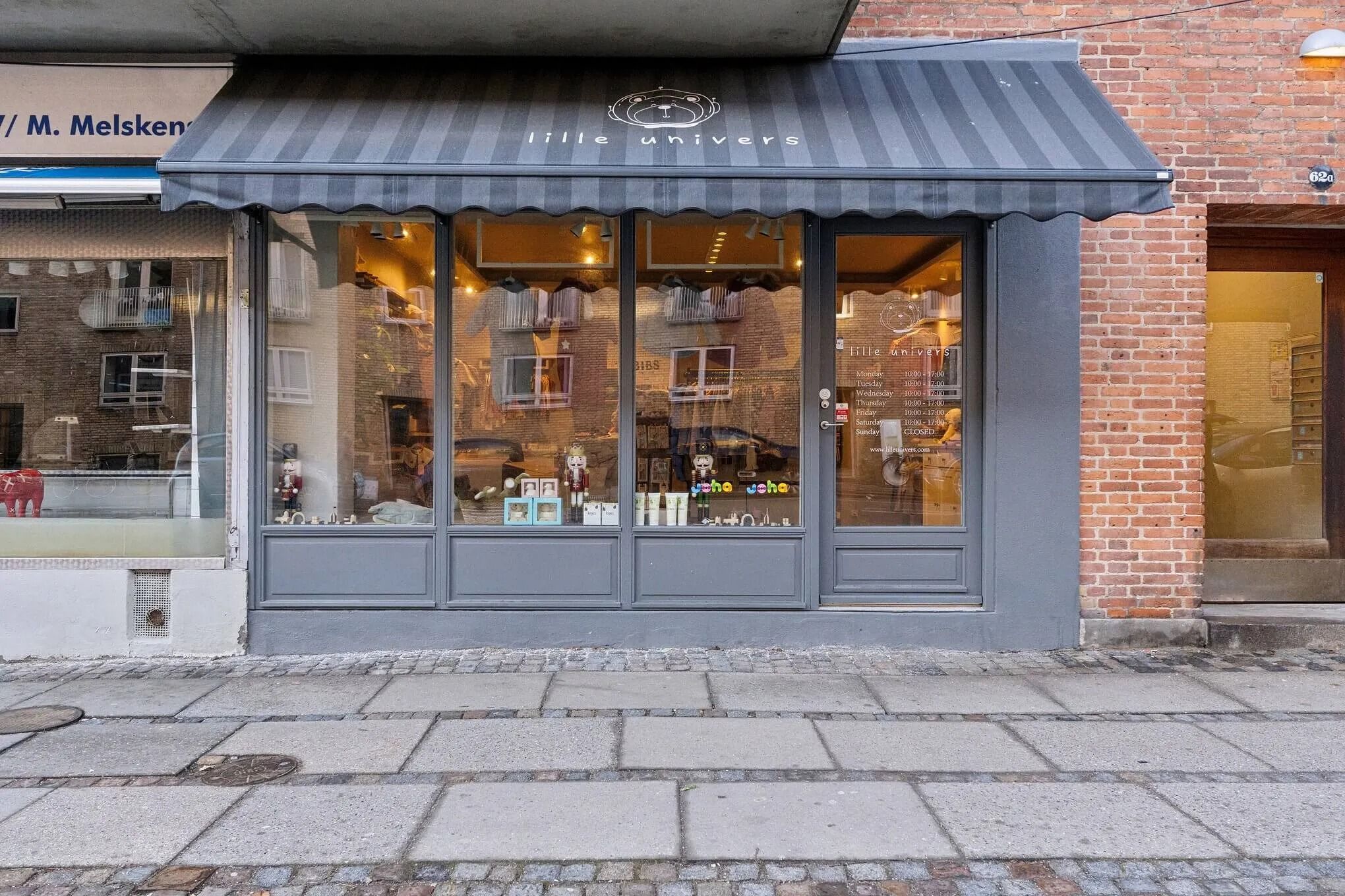 Lille Univers butik med sort laftet skur og glasvinduer og indvendige produkter i udsalgsvindue