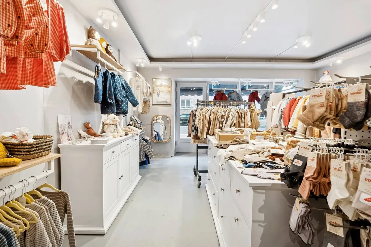 Butik med smukke klæder og tøj til babyer og småbørn, lyse loftslamper og en spissende hylde med tøj
