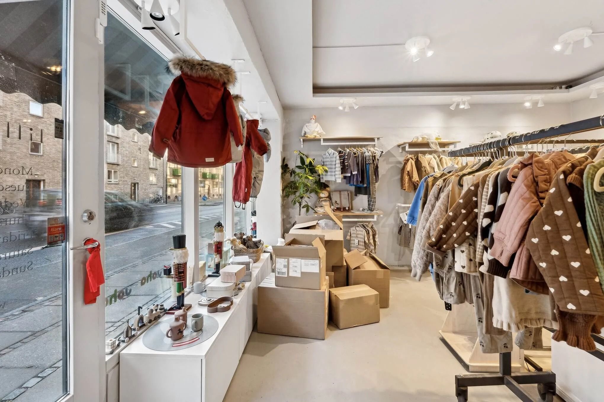 Butik med tøj, der er hængt op i en stor række, og tøj er pakket i kasser og placeret på gulvet. Også tøj er hængt op i