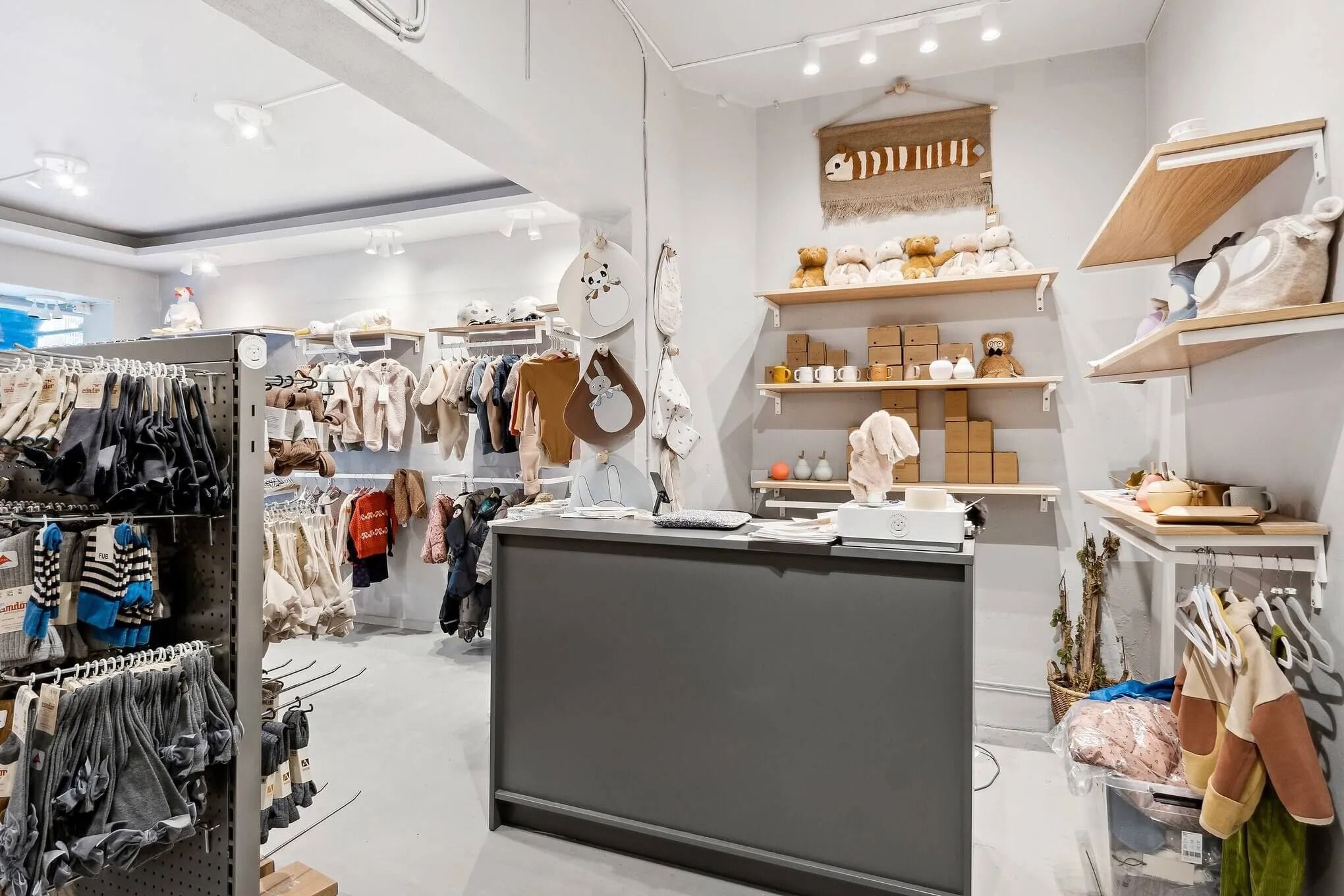 Sort og hvidt indrettet butik med børnetøj, tøjstative, og et baglokale med eksemplarer af børnetøj og diverse varer på