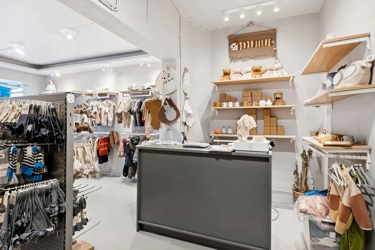 Sort og hvidt indrettet butik med børnetøj, tøjstative, og et baglokale med eksemplarer af børnetøj og diverse varer på