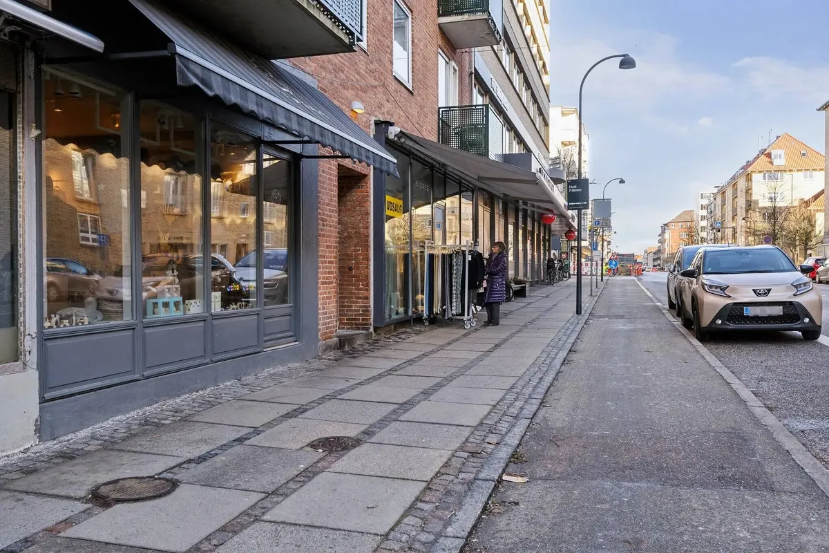 Mennesker går på gågaden i København, og en Toyota Corolla er parkeret langs vejen. Der er flere butikker med skilte og