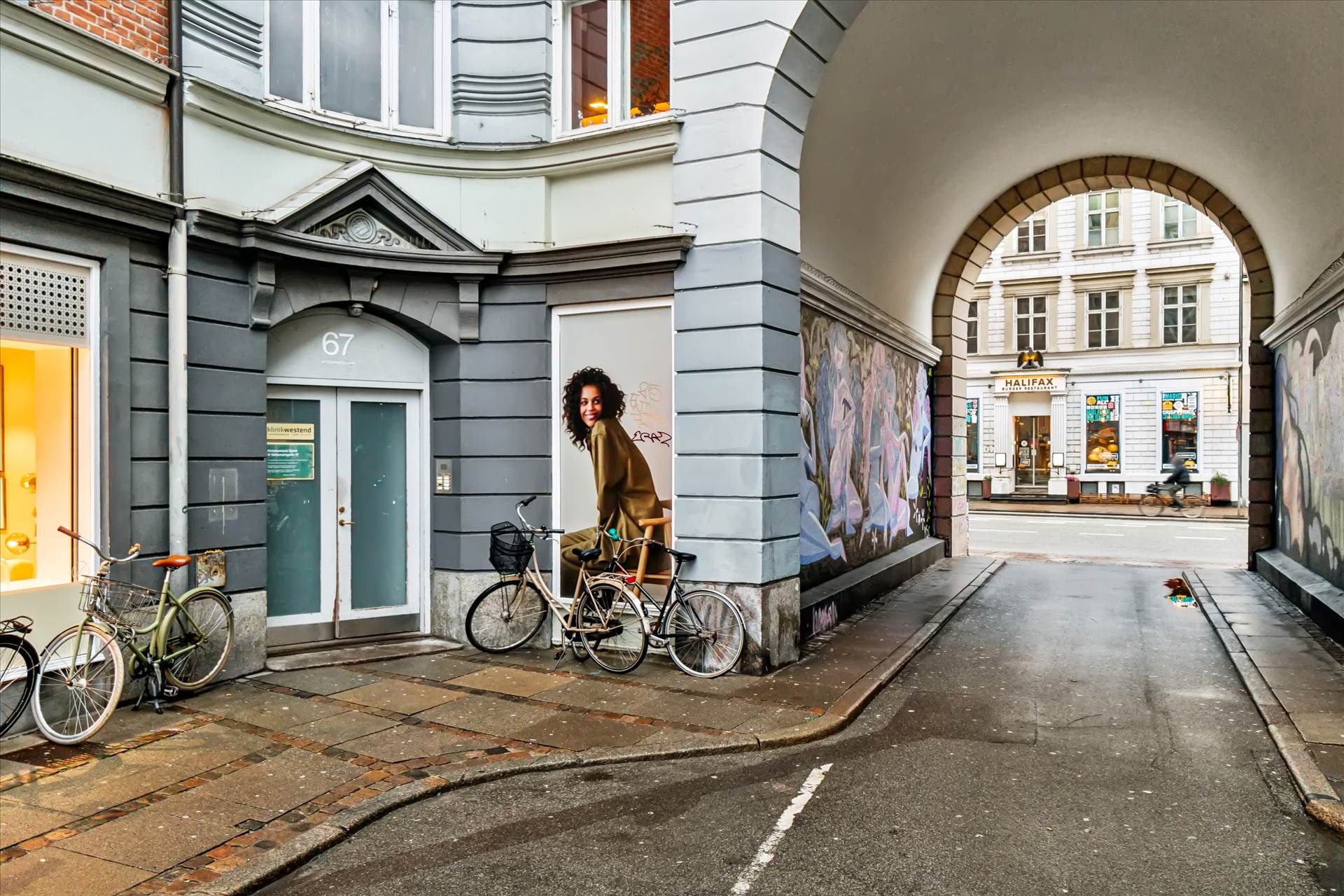 To cykler med kurve parkeret udenfor 67, graffiti på væggen og en kvinde i et maleri