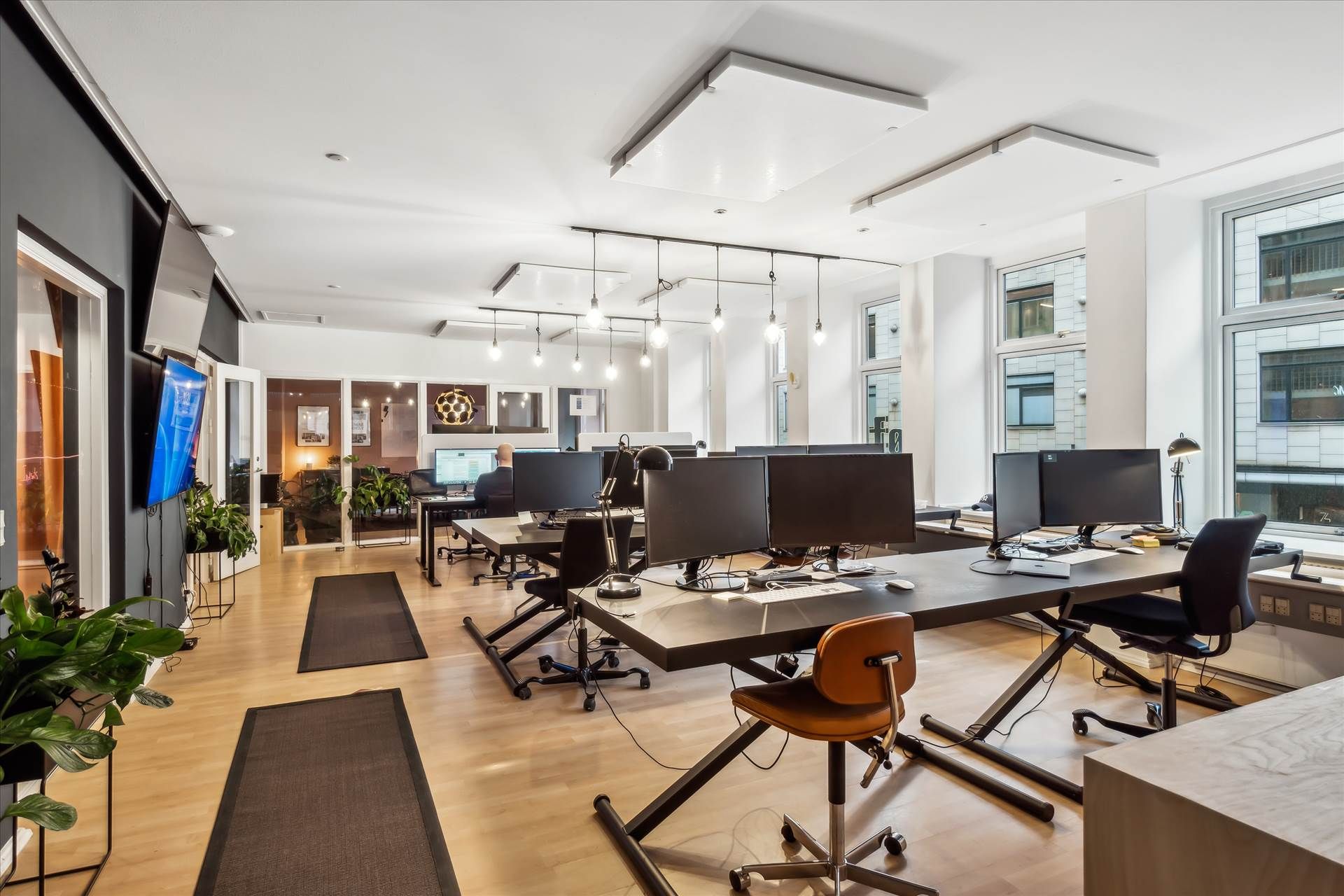 Kontor med trægulve, moderne skriveborde, lysekroner og vinduer, der giver god udsigt til byen