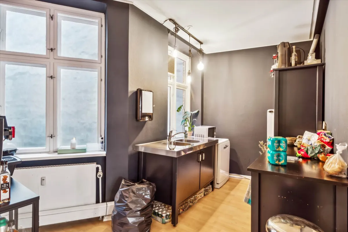 Alt i et lille køkken med højt til loftet, trægulv, dobbelt vask og mikrobølgeovn samt køleskab og ovn