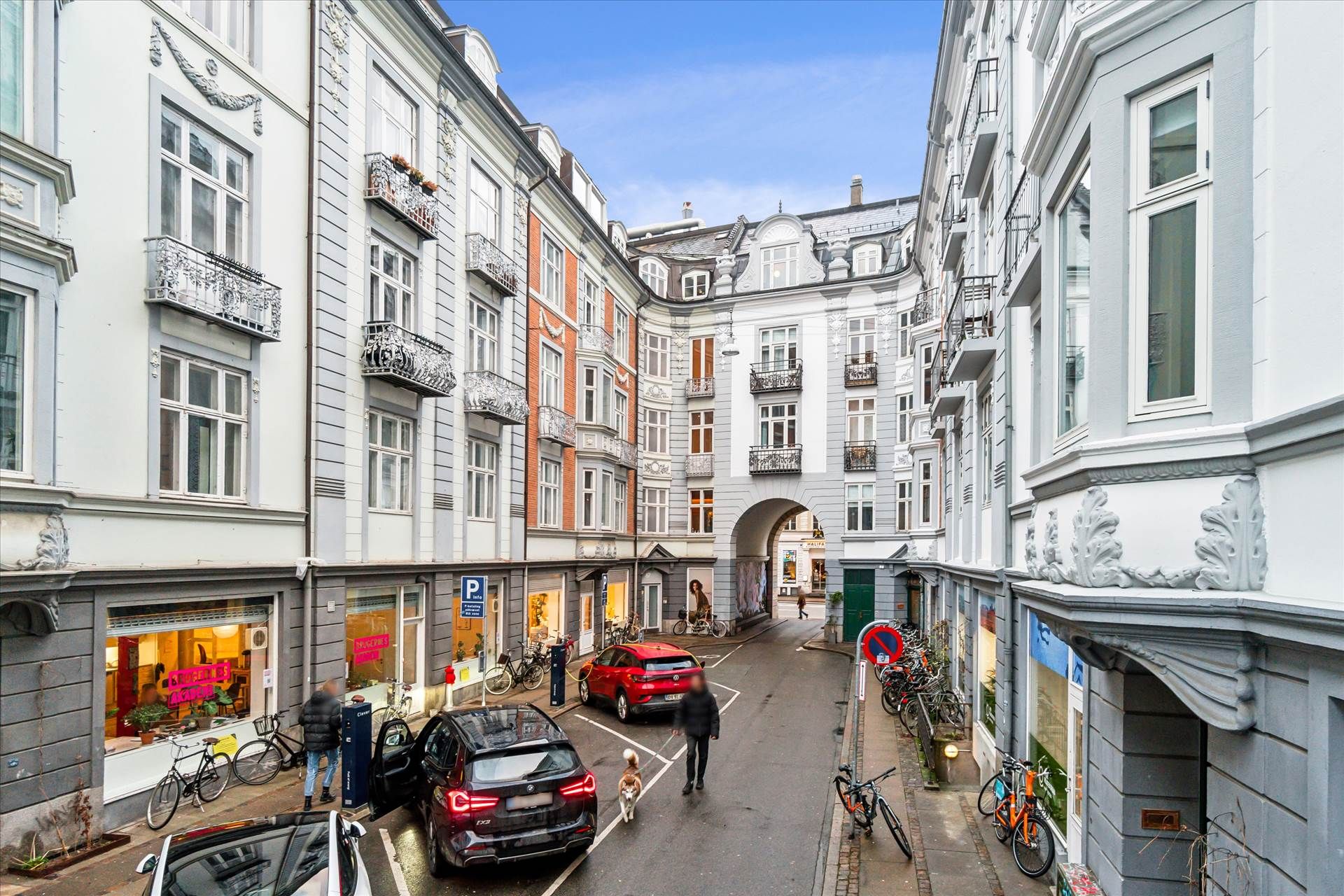 Forskudtaget parkerede biler udenfor, slanke træhusbygninger og enkeltgående personer med hund på Frederiksberg i København