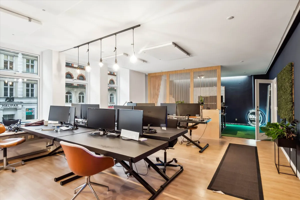 Moderne kontor med lyse gulve, bord med computere og skrivebordsstole samt lyse loftslys og træindslag