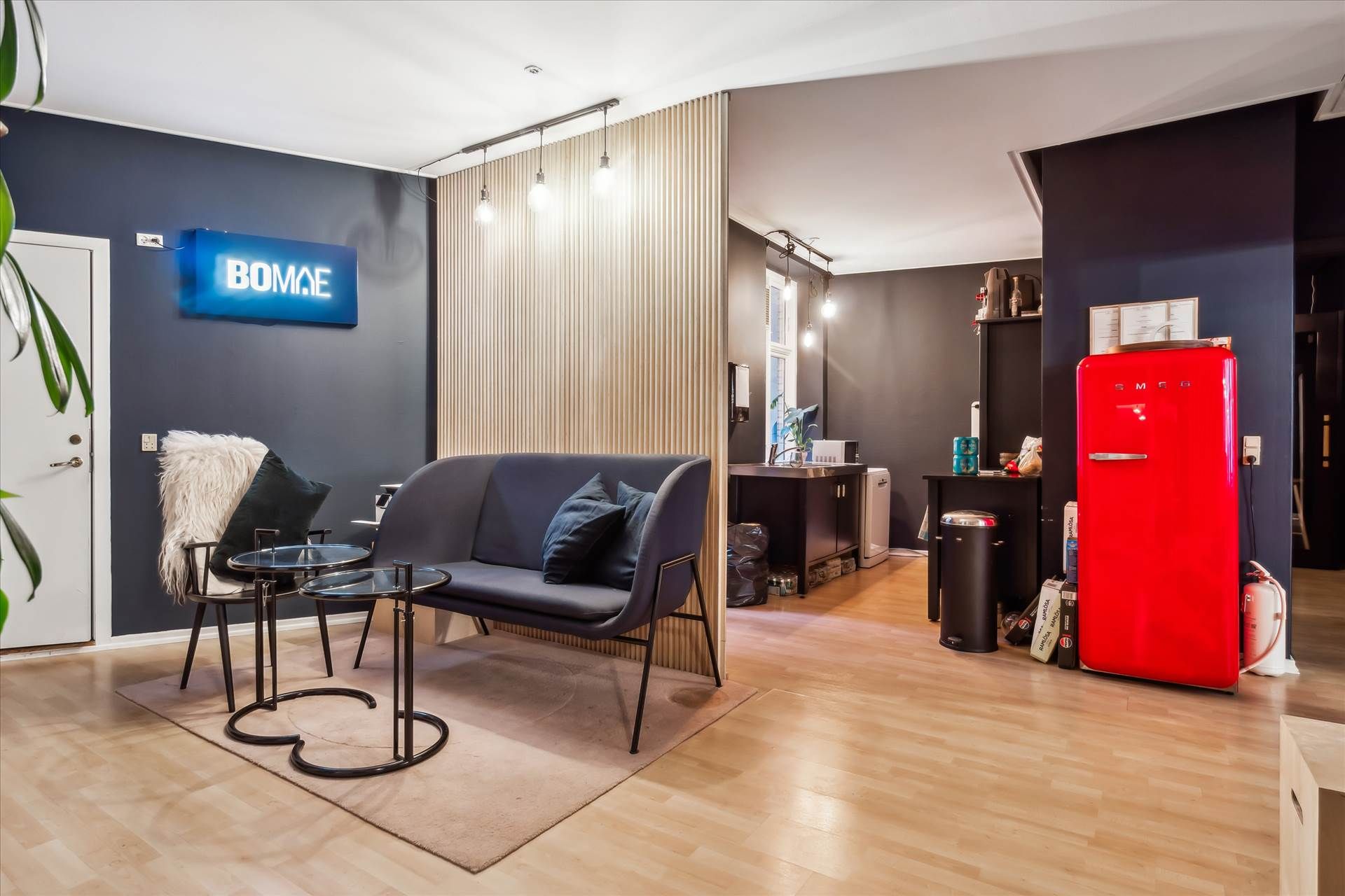 Moderne lejlighed med lysegule vægge, trægulv og blå sofa med puder, to bord og en rød køleskab