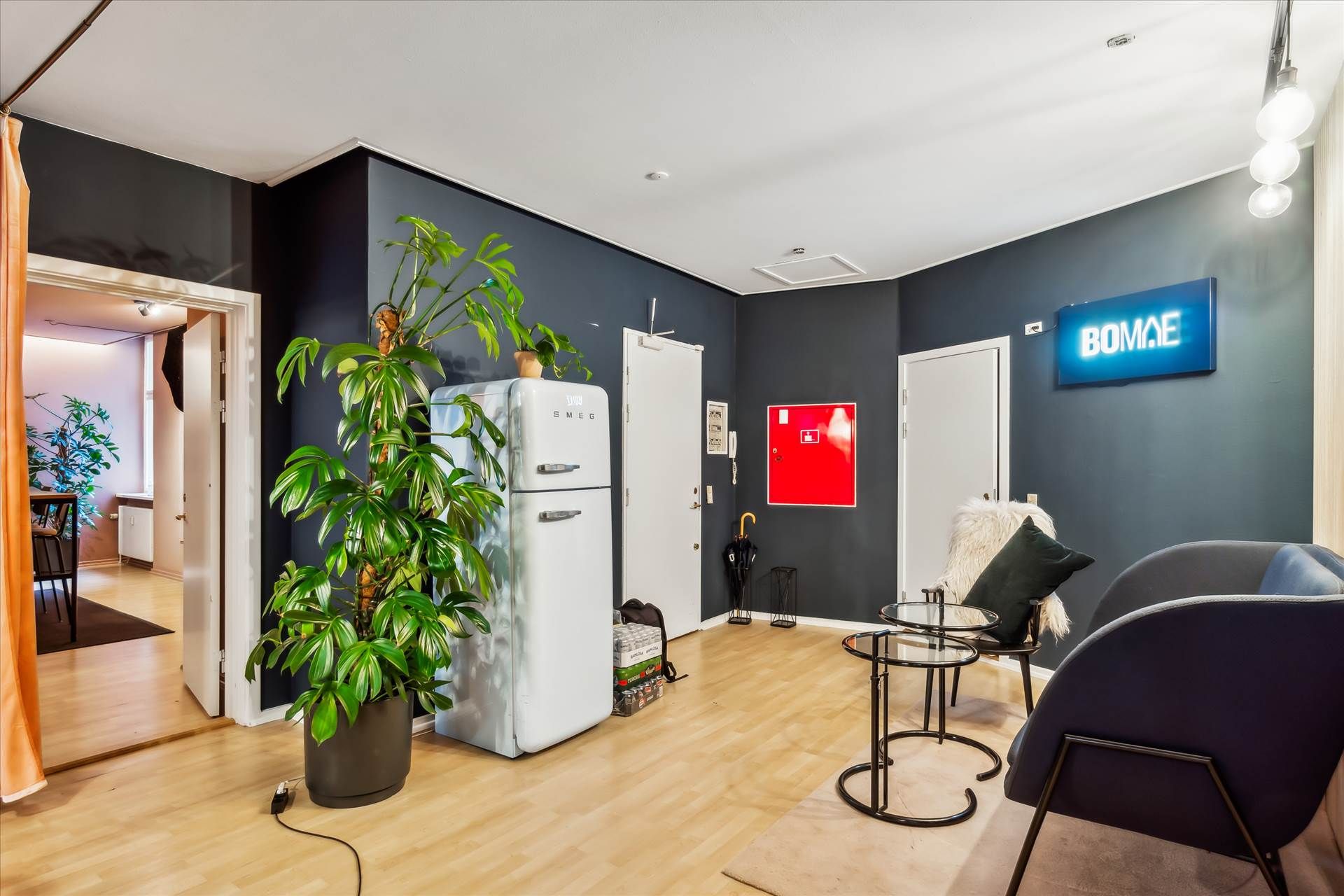 På billedet ses et moderne interiør med højloftede rum og pæne trægulve. Der er en hvid køleskab og en stor grøn plante. Et