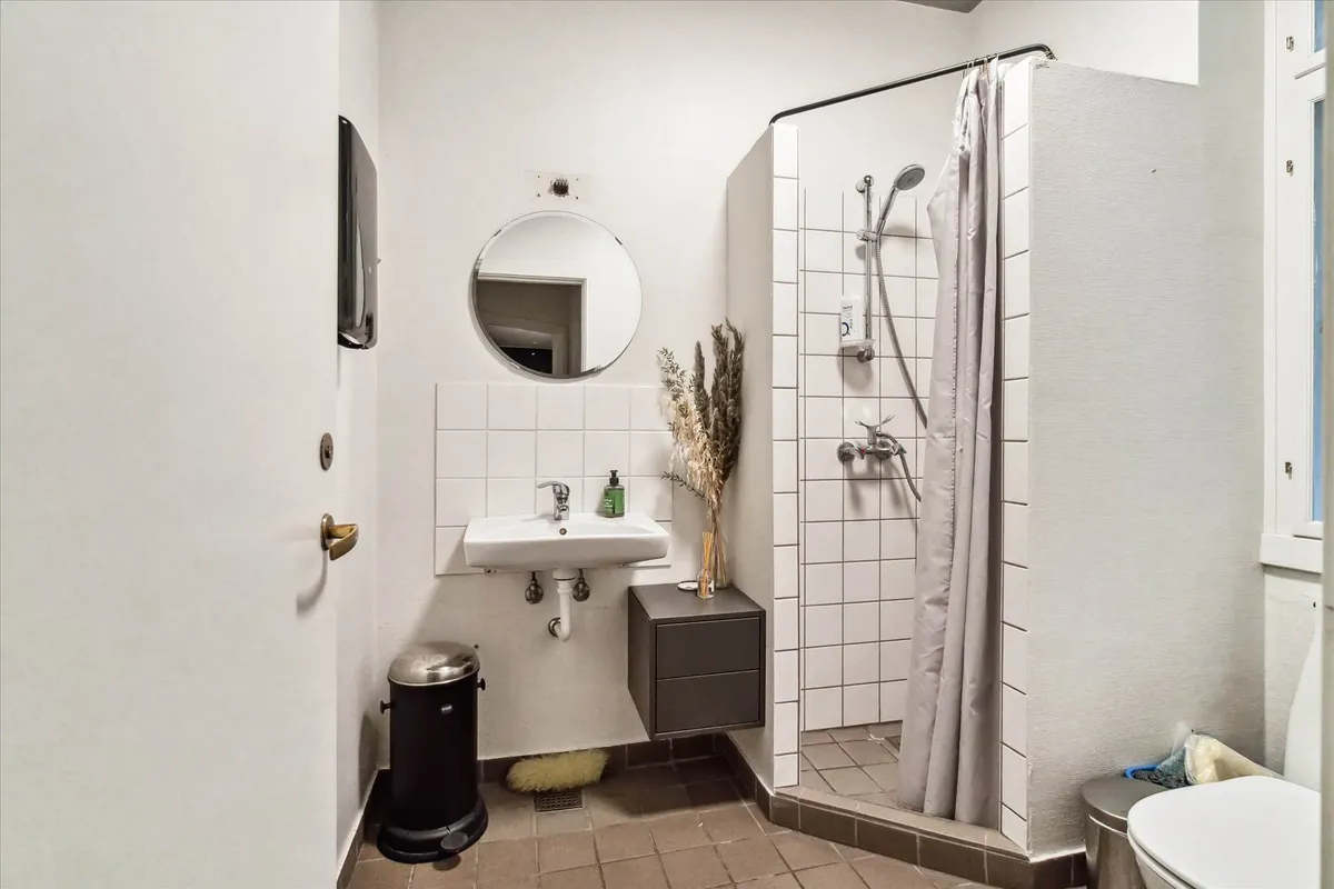 En moderne hvidt interiør med en høj toilet, badeværelse med en brusekabine, et spejl og en håndvask