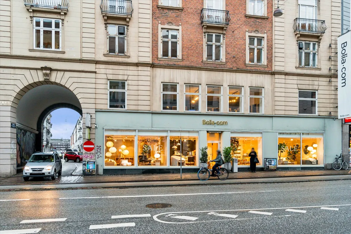 Personer går forbi en Bolia.com butik, som har udsalg i vinduet. To personer cykler forbi og en person står foran butikken.