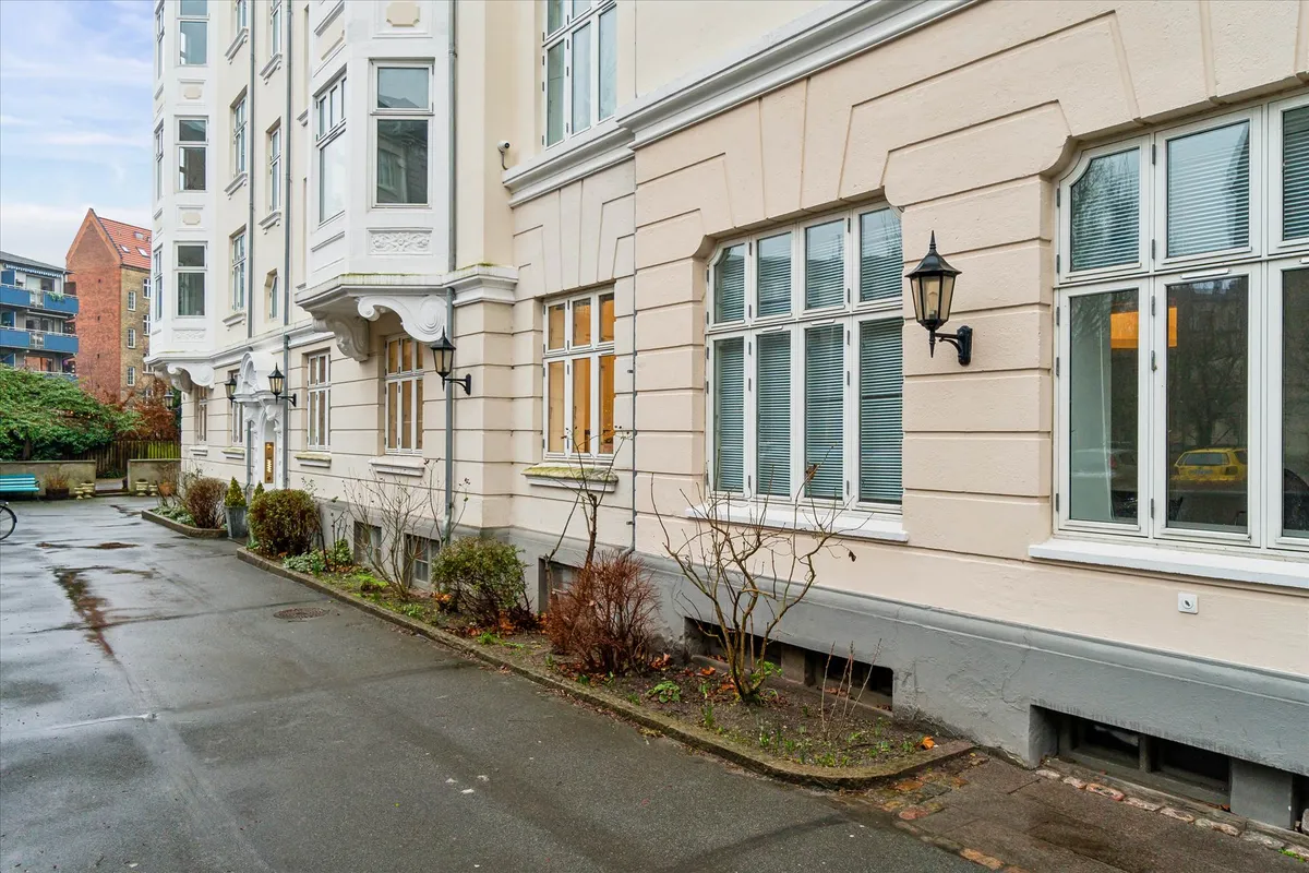 Rolig beliggenhed med flot indgangsparti og smuk hvidpudsede bygning med lyse ruder og hjørnehaven i forgrunden